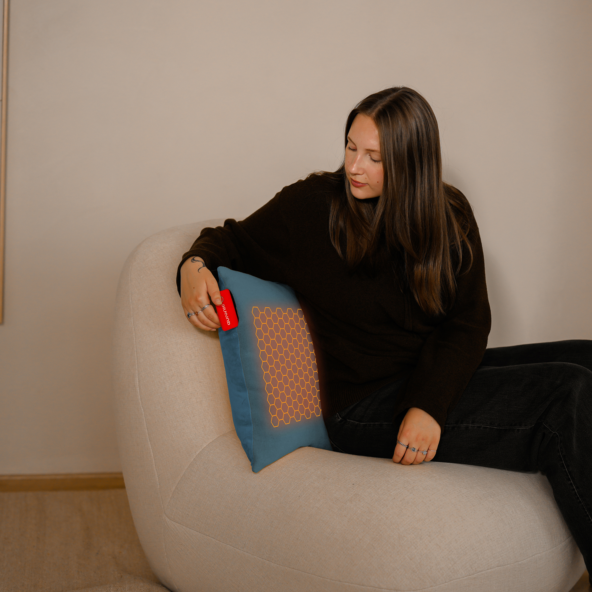 Femme assise sur une chaise avec un coussin chauffant sur un oreiller. Elle tient un appareil de contrôle rouge.
