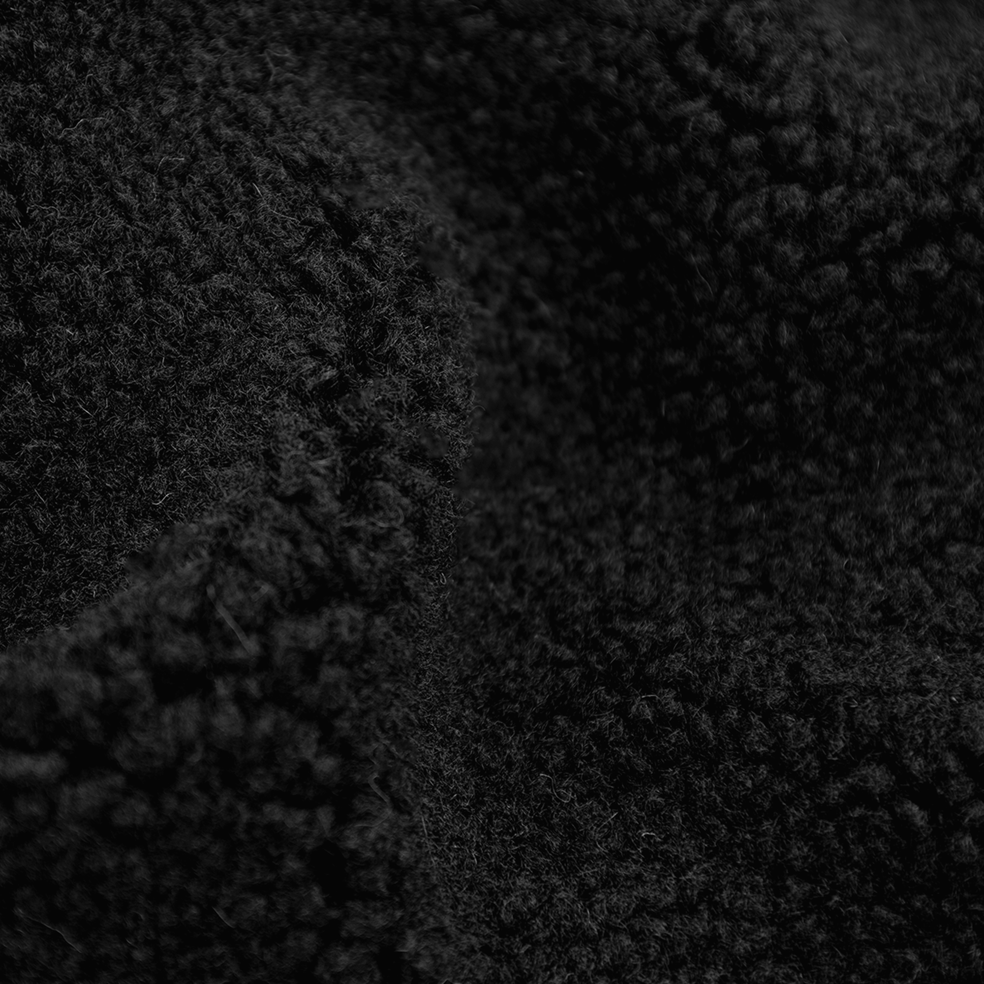 Gros plan sur un tissu noir texturé. La surface est dense, avec un aspect doux et flou, et quelques plis.