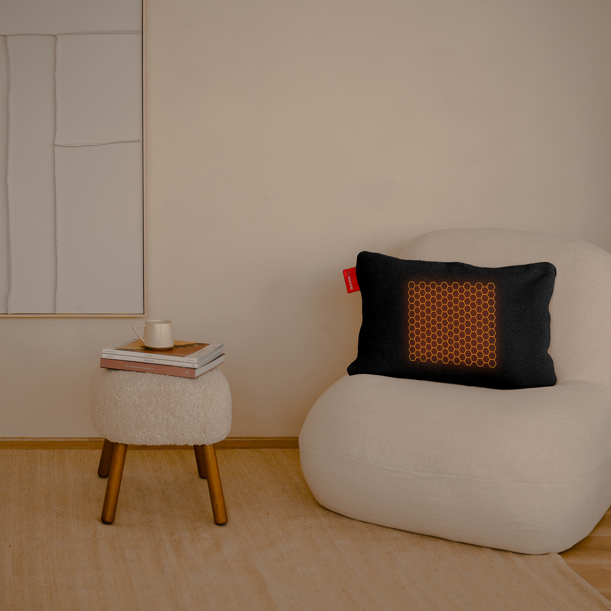 A black pillow with a honeycomb design sits on a white chair. A small stool holds books and a mug.