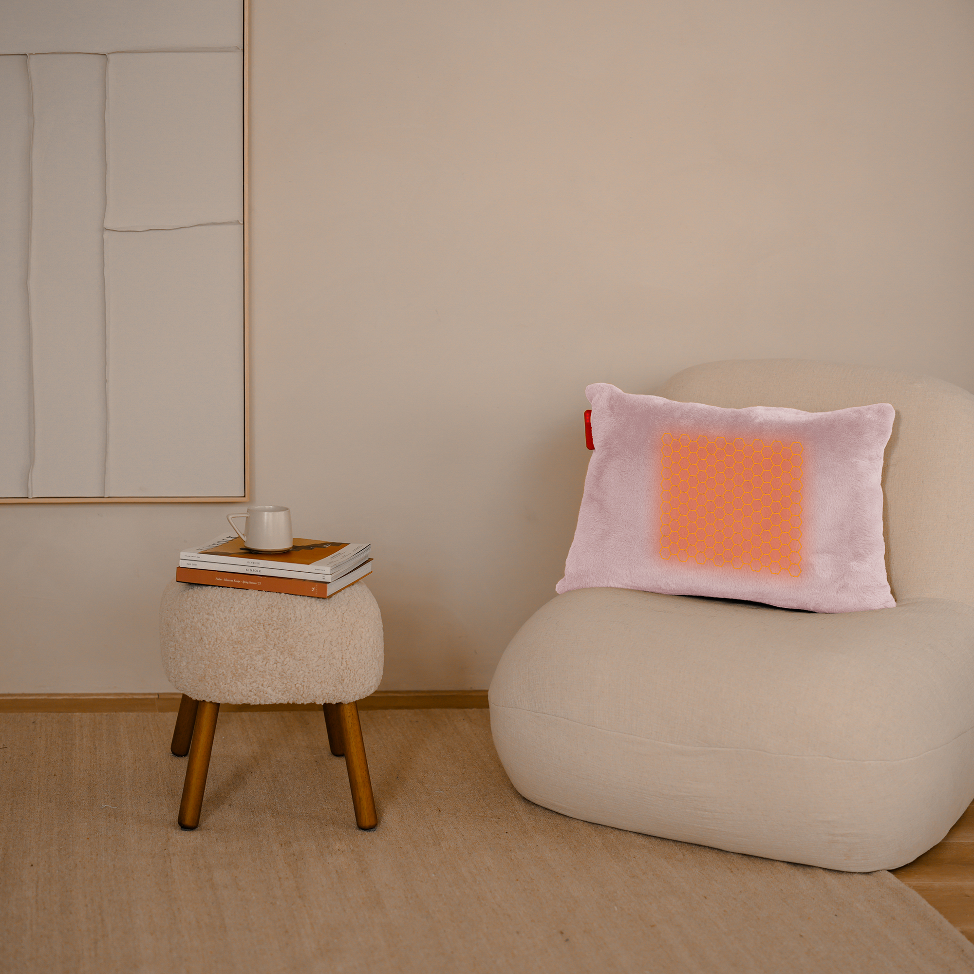 Une scène de chambre. Un oreiller rose avec un motif orange sur une chaise blanche. Un tabouret avec des livres et une tasse à côté.