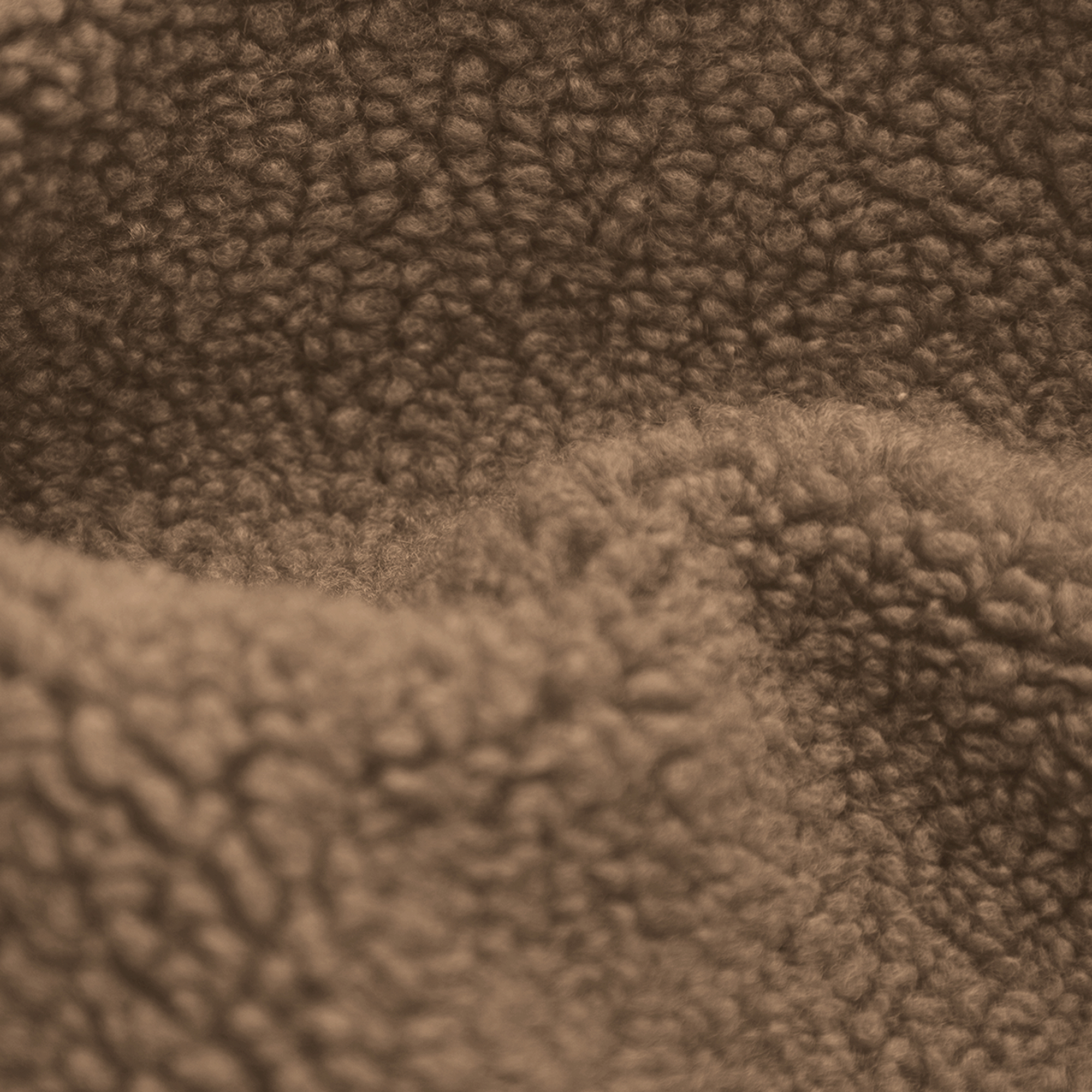 Close-up van bruine, zachte stof. De textuur heeft veel kleine, afgeronde bobbels, wat een zachte, warme uitstraling creëert.