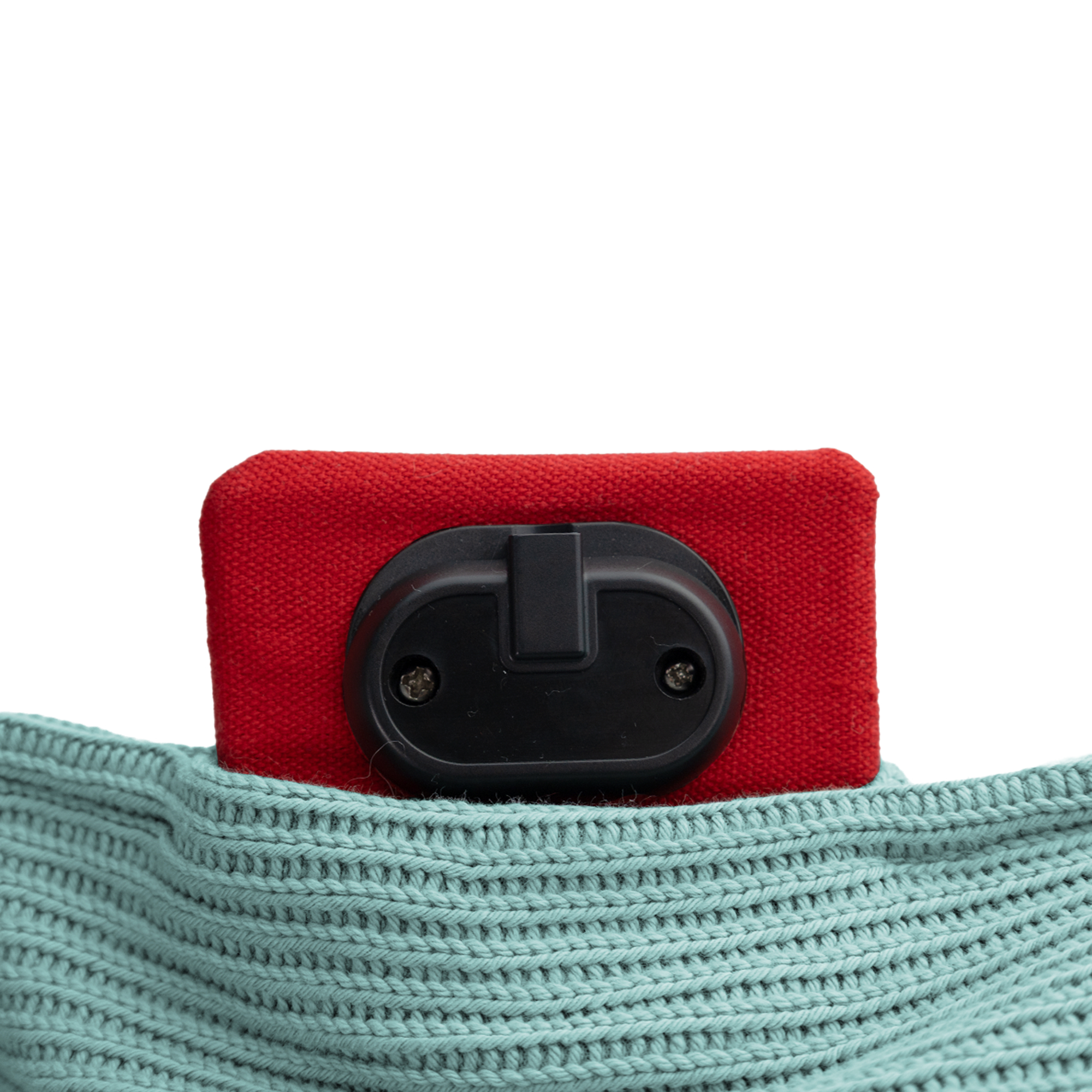 Een rood object met een zwart onderdeel is gedeeltelijk zichtbaar, rustend op een lichtblauwe gebreide stof, tegen een witte achtergrond.