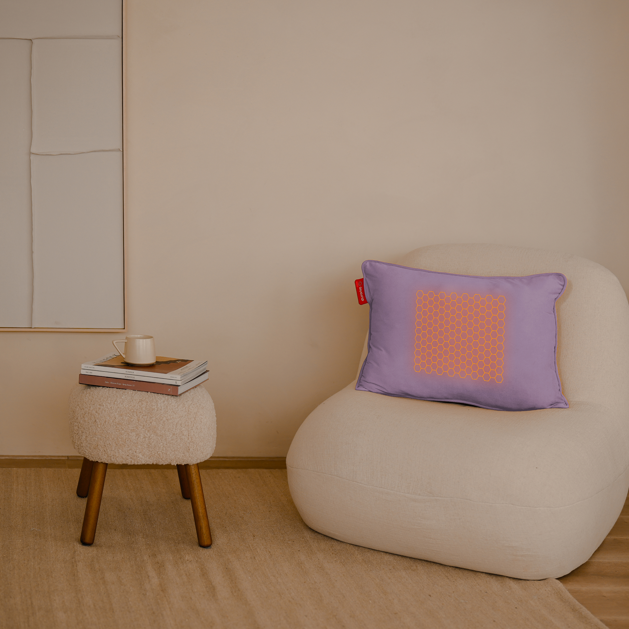 Een gezellige kamer met een beige fauteuil, een krukje met boeken en een mok, en een kussen met een oranje honingraatpatroon.