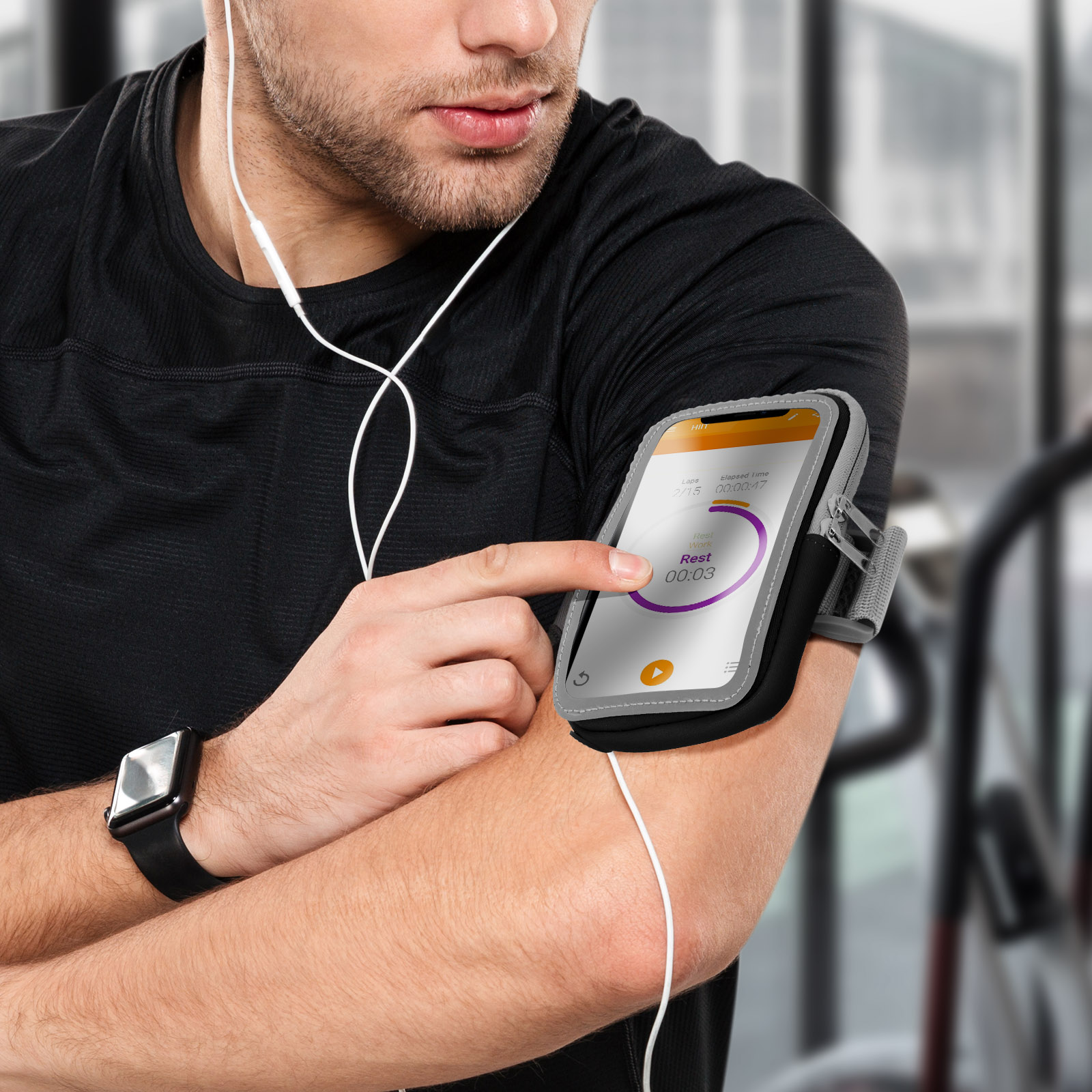 Homme en chemise noire utilise un téléphone avec une application d'entraînement. Il porte une montre et un brassard. Écouteurs utilisés.