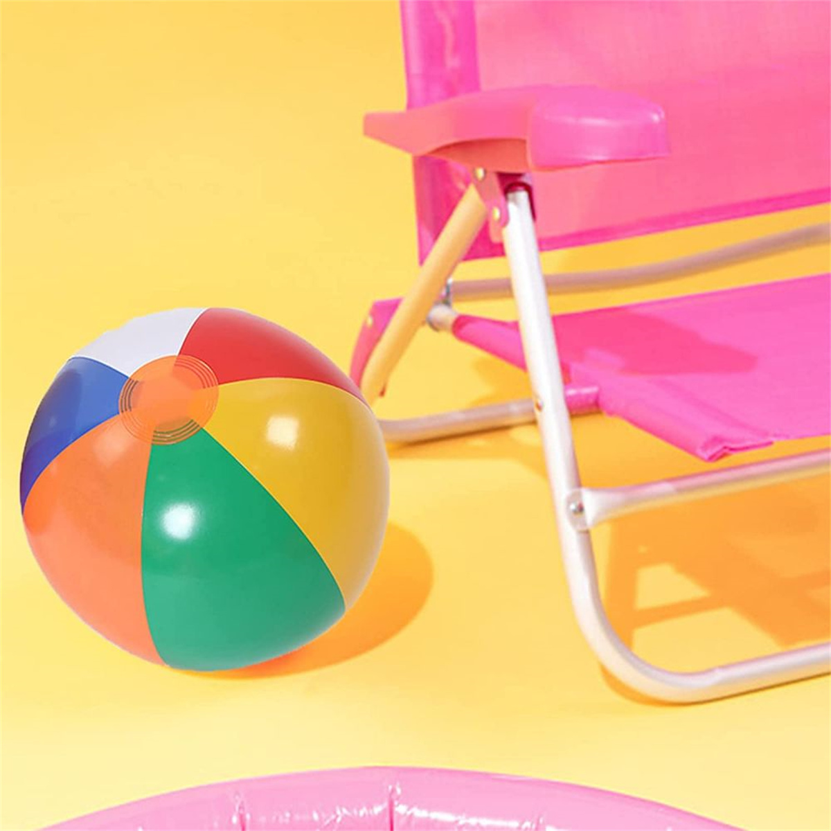 Ein bunter Strandball liegt in der Nähe eines rosa Strandstuhls auf gelbem Grund. Die Szene deutet auf einen sonnigen Tag am Strand hin.
