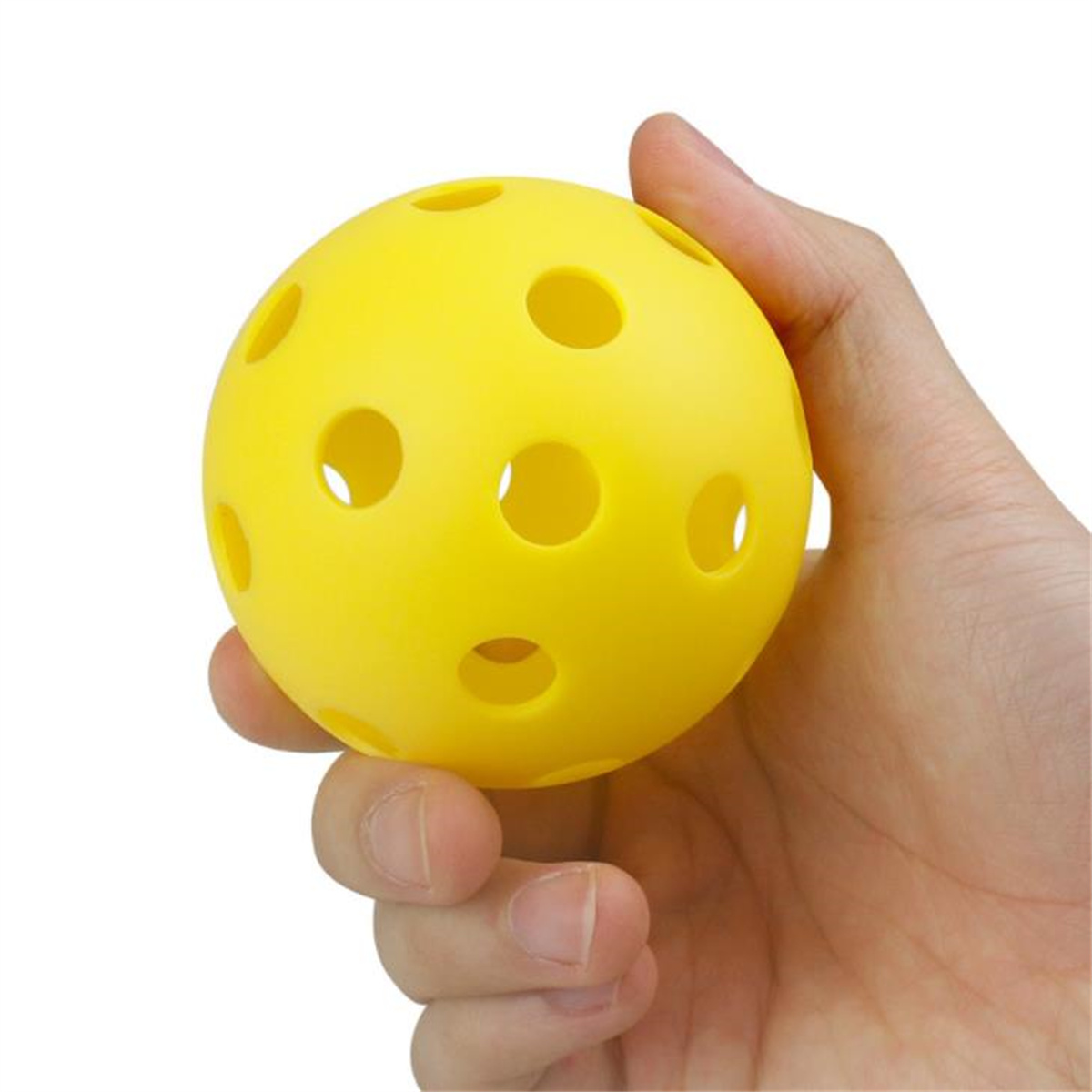 Eine Hand hält einen gelben Ball mit Löchern. Der Ball ist rund und glatt. Der Hintergrund ist weiß.