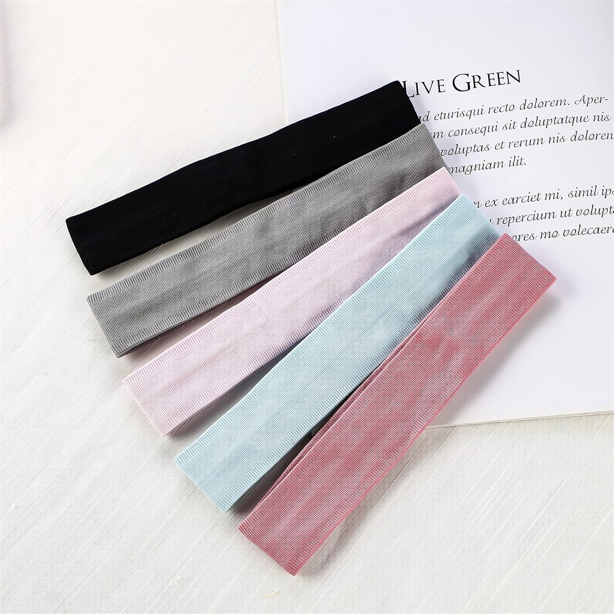 Fünf bunte Stirnbänder in Schwarz, Grau, Rosa, Hellblau und Rot, diagonal auf einer weißen Oberfläche angeordnet.