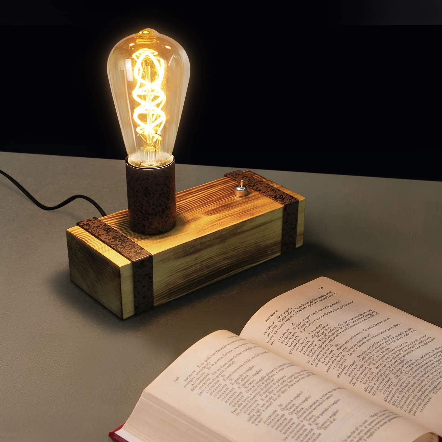 Una lampada con lampadina Edison accesa su una scatola di legno. Un libro aperto è sul tavolo. Lo sfondo è scuro.