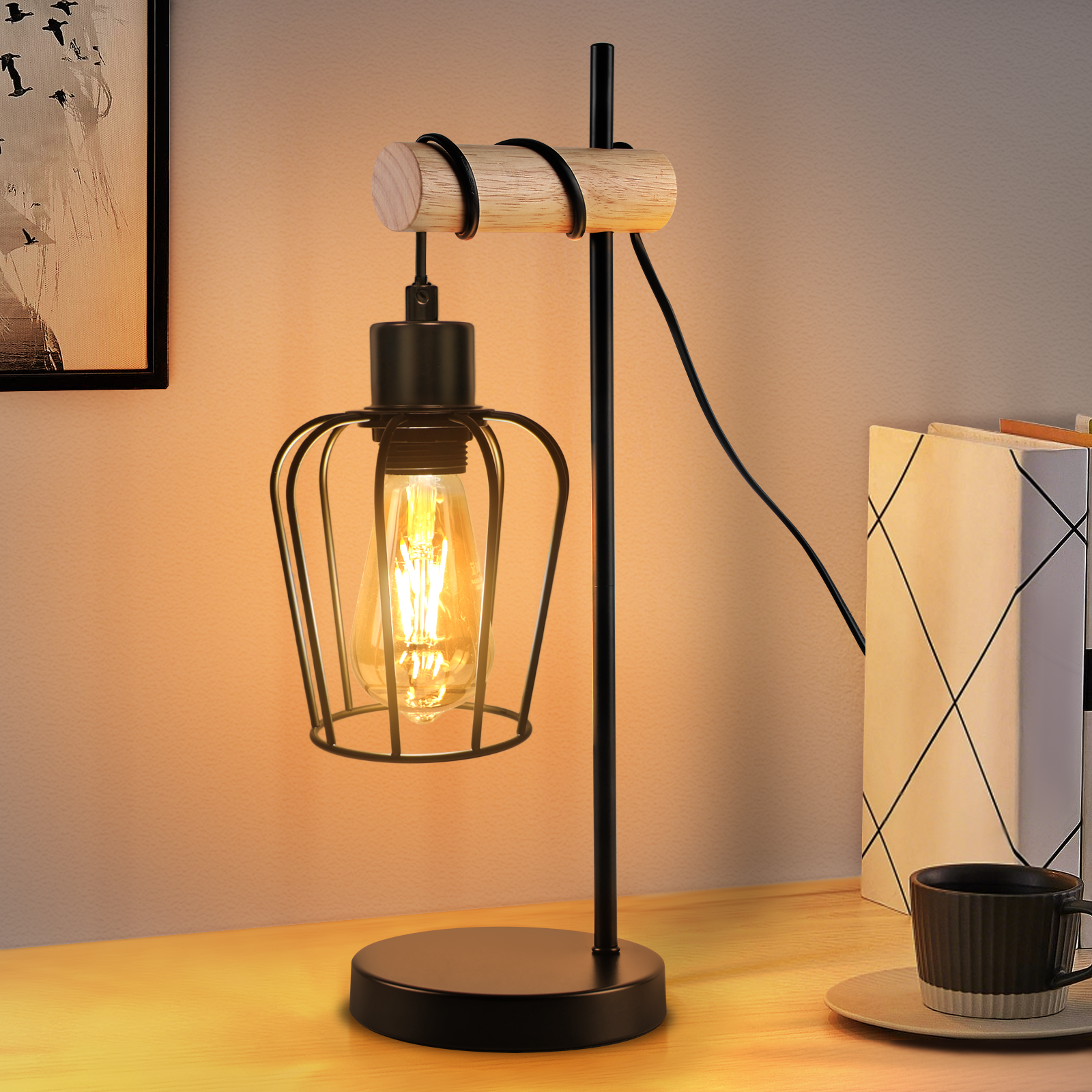 Una lampada da scrivania nera con paralume a gabbia e lampadina a vista. Si trova su una superficie di legno, accanto a una tazza di caffè e libri.