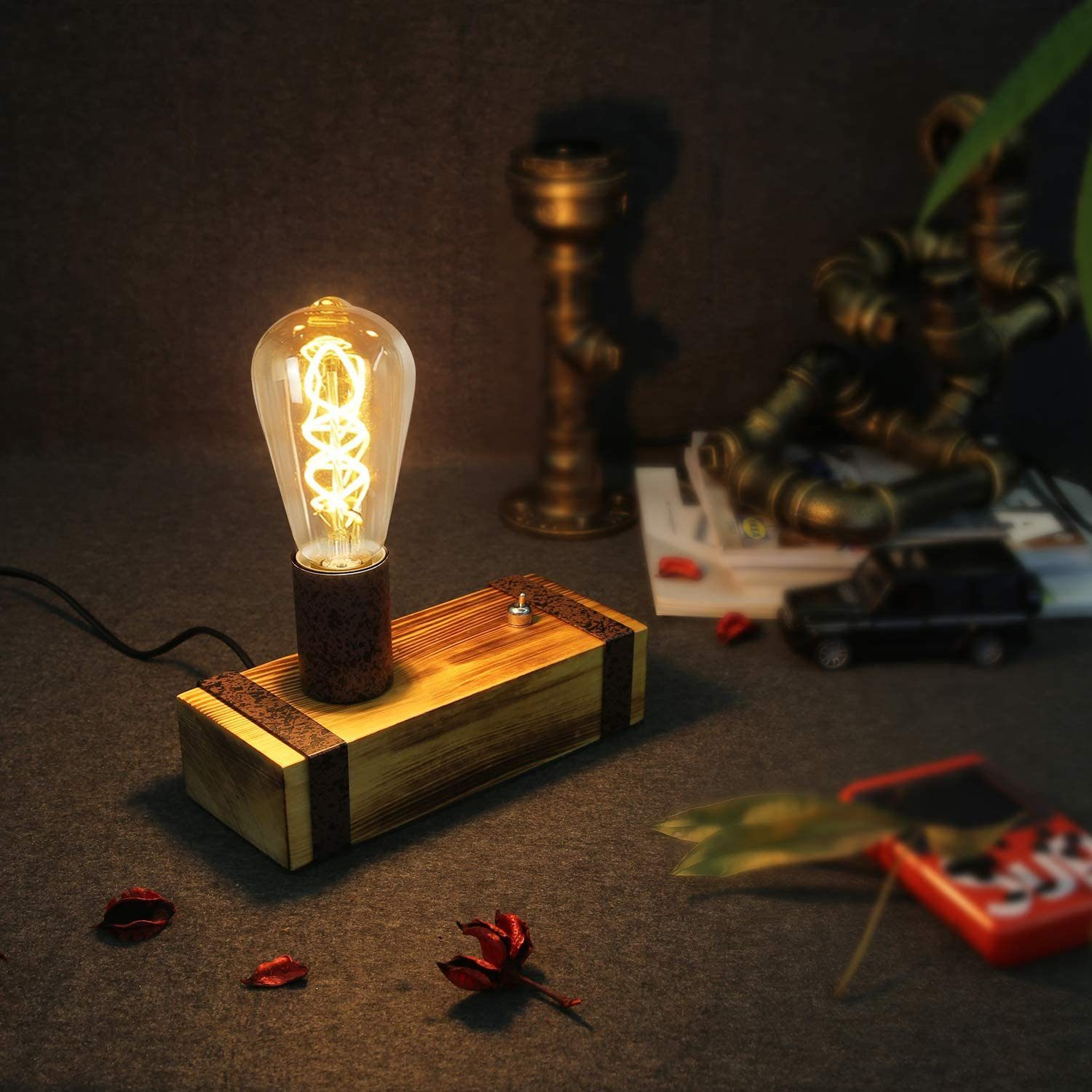 Una lampada con lampadina Edison accesa su una scatola di legno. Un'auto modello, tubi e foglie rosse sullo sfondo.