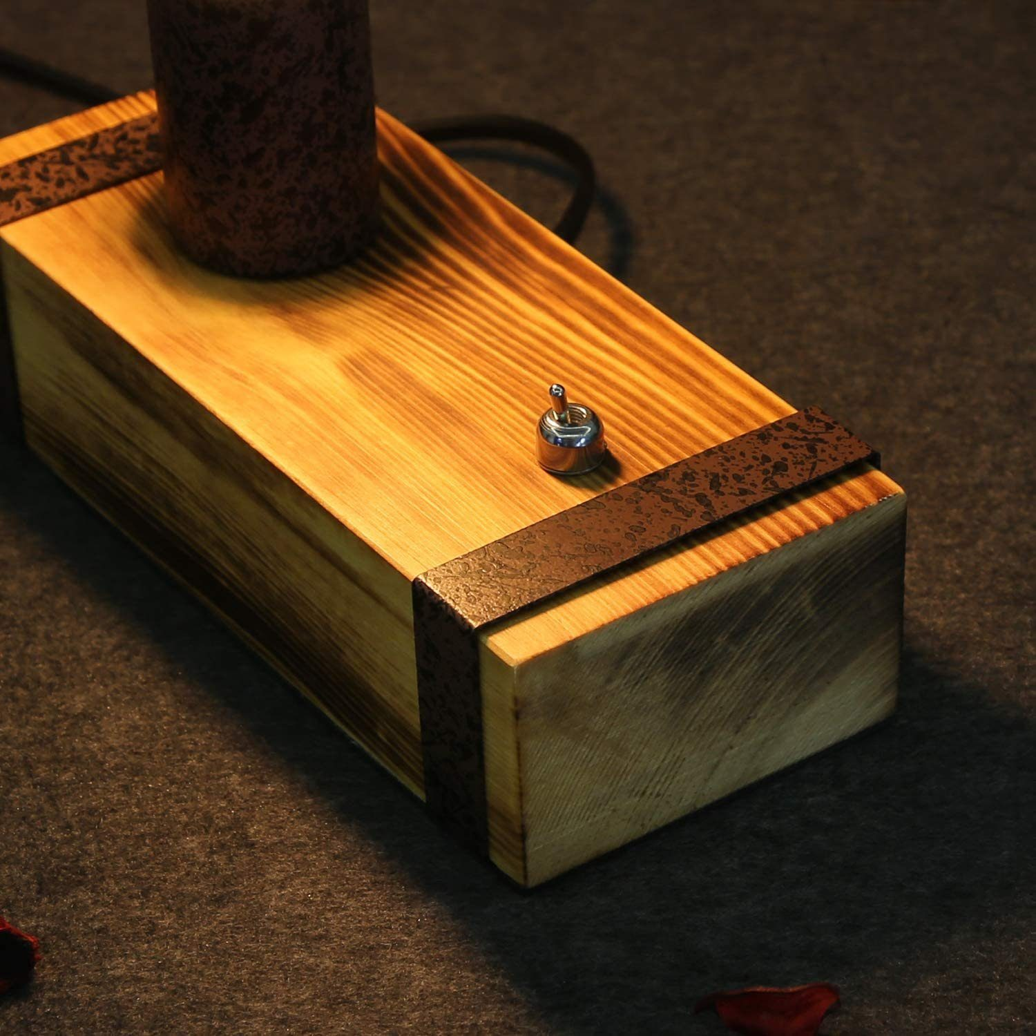 Base lampada in legno con candela marrone e interruttore. La base è rettangolare con cinghie metalliche e lo sfondo è scuro.