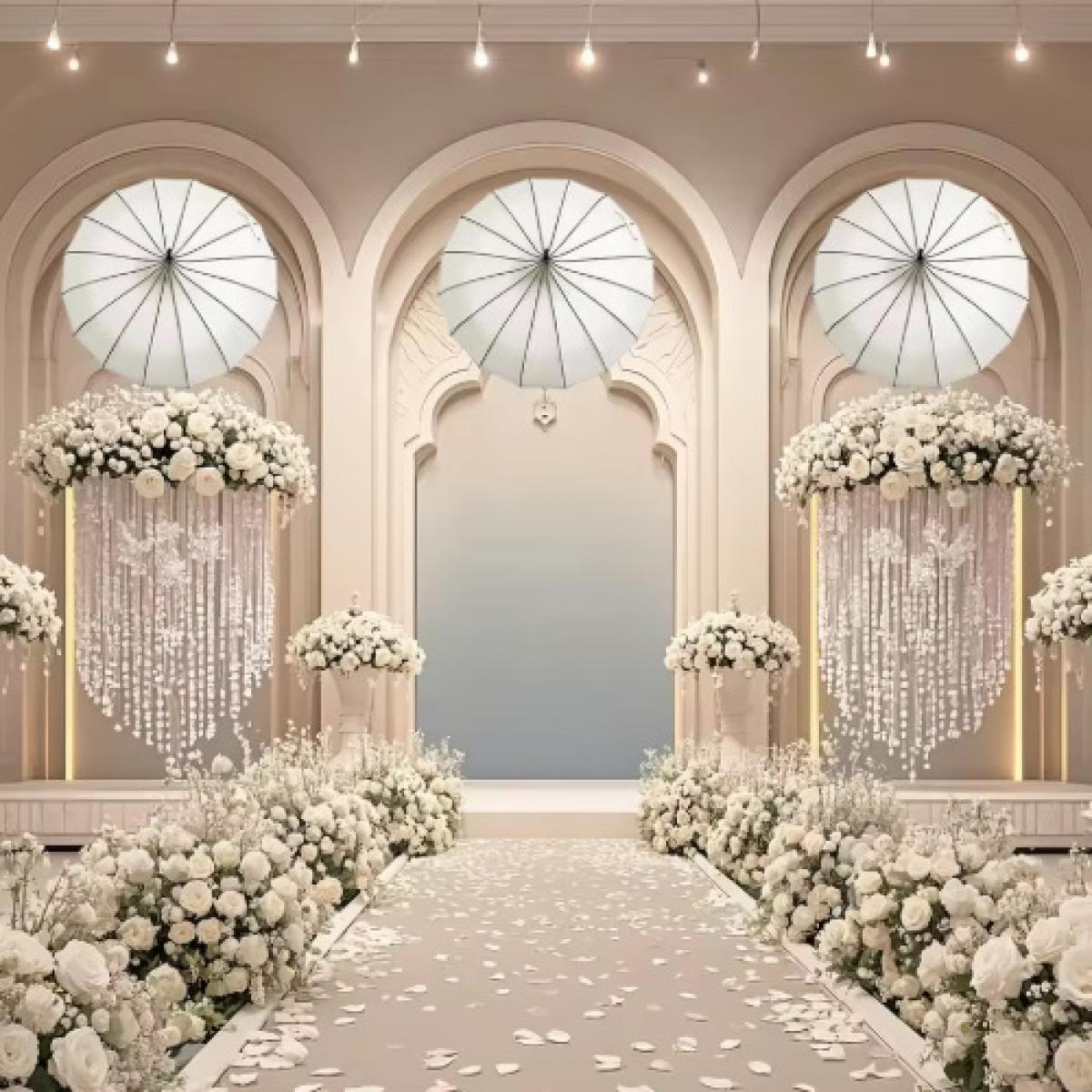 Eine Hochzeitsszene mit weißen Blumen, Bögen und Schirmen. Gang mit Blütenblättern. Blumenschmuck und hängende Kristalle schmücken den Veranstaltungsort.