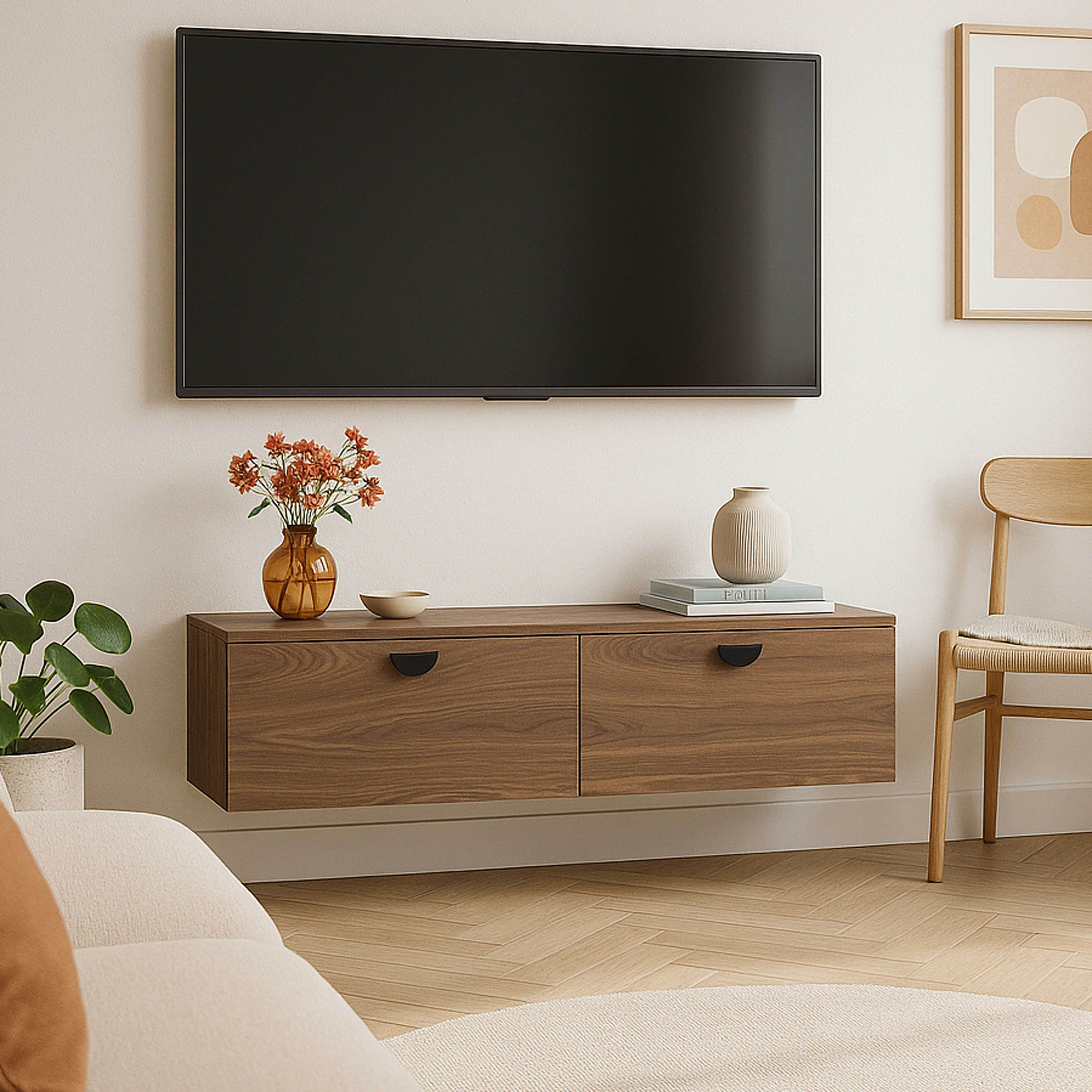 Ein an der Wand montierter Fernseher über einem Holzschrank mit Blumen. Ein Stuhl und eine Topfpflanze befinden sich an den Seiten.