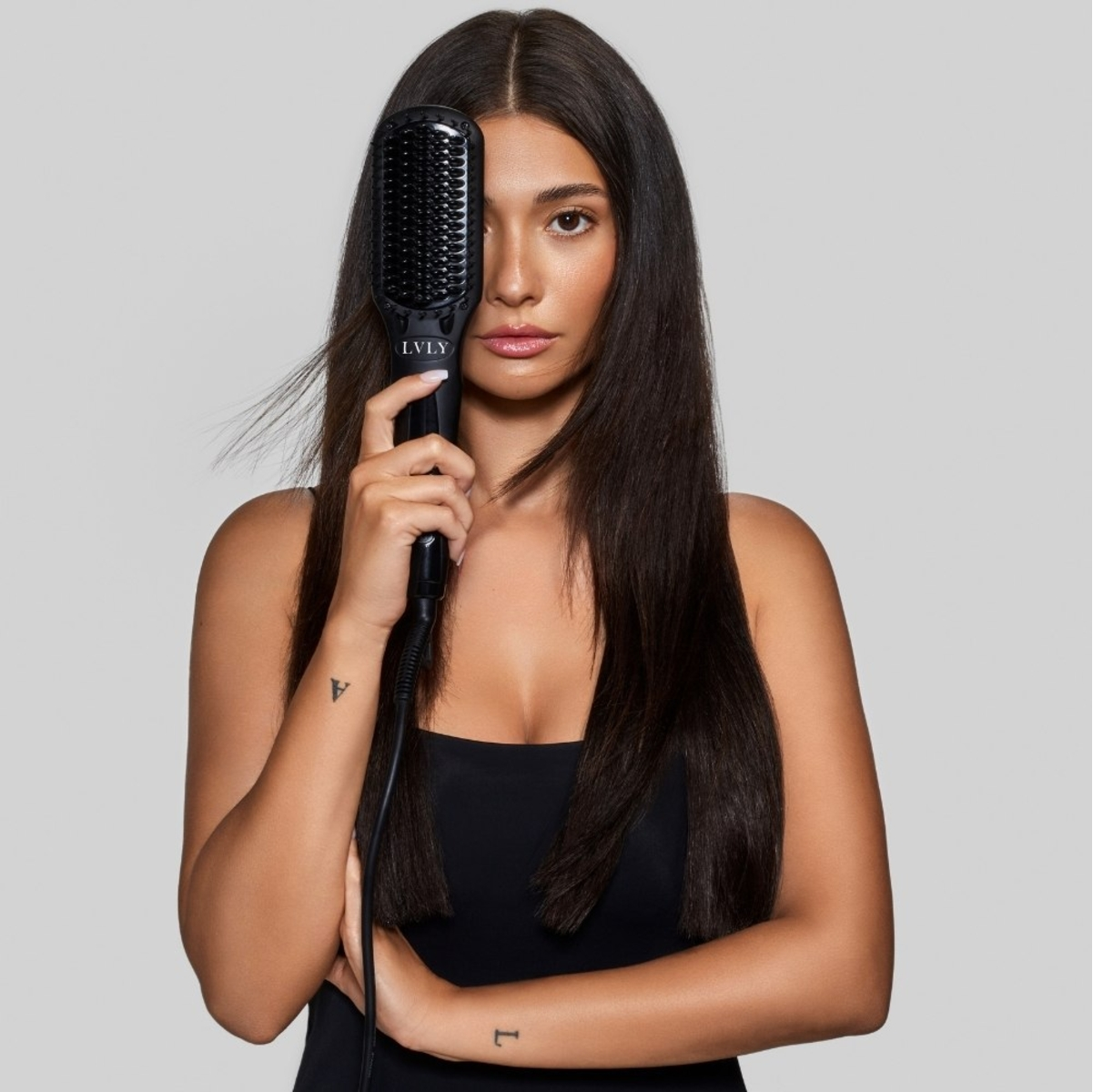 Eine Frau hält eine Haarglättungsbürste vor ihr Gesicht. Sie trägt ein schwarzes Oberteil und hat lange, dunkle Haare.