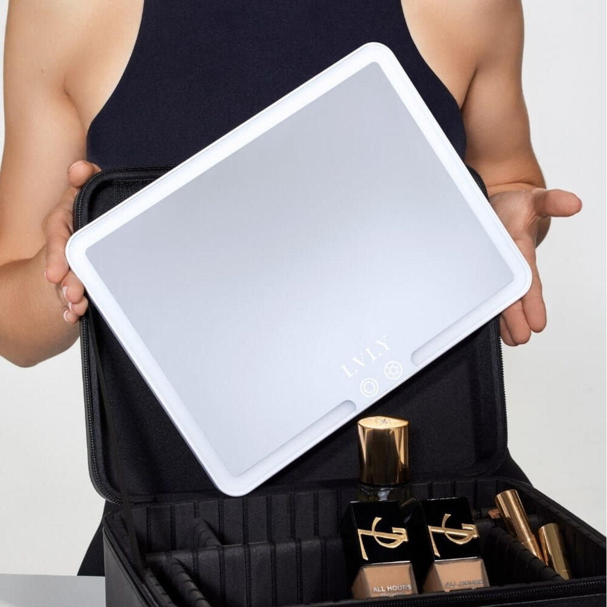 Eine Person hält einen beleuchteten weißen Schminkspiegel über einer offenen schwarzen Schminktasche. Die Tasche enthält Make-up-Produkte.
