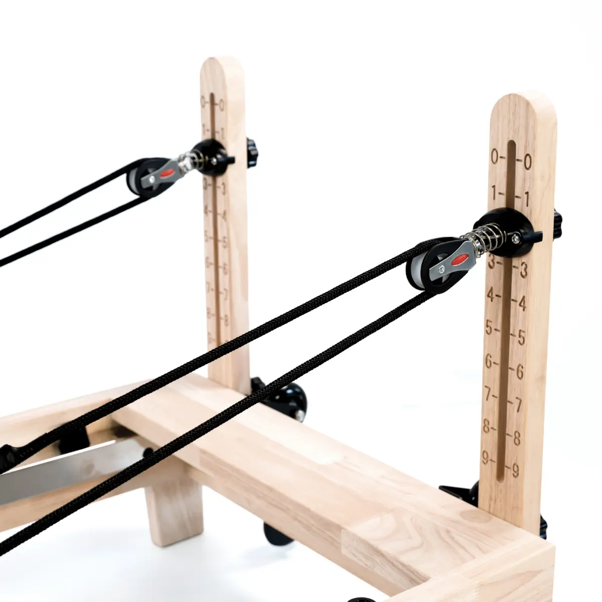 Houten Pilates-machine met zwarte touwen en katrollen. Verticale houten steunen met genummerde markeringen. Licht hout en zwarte accenten.