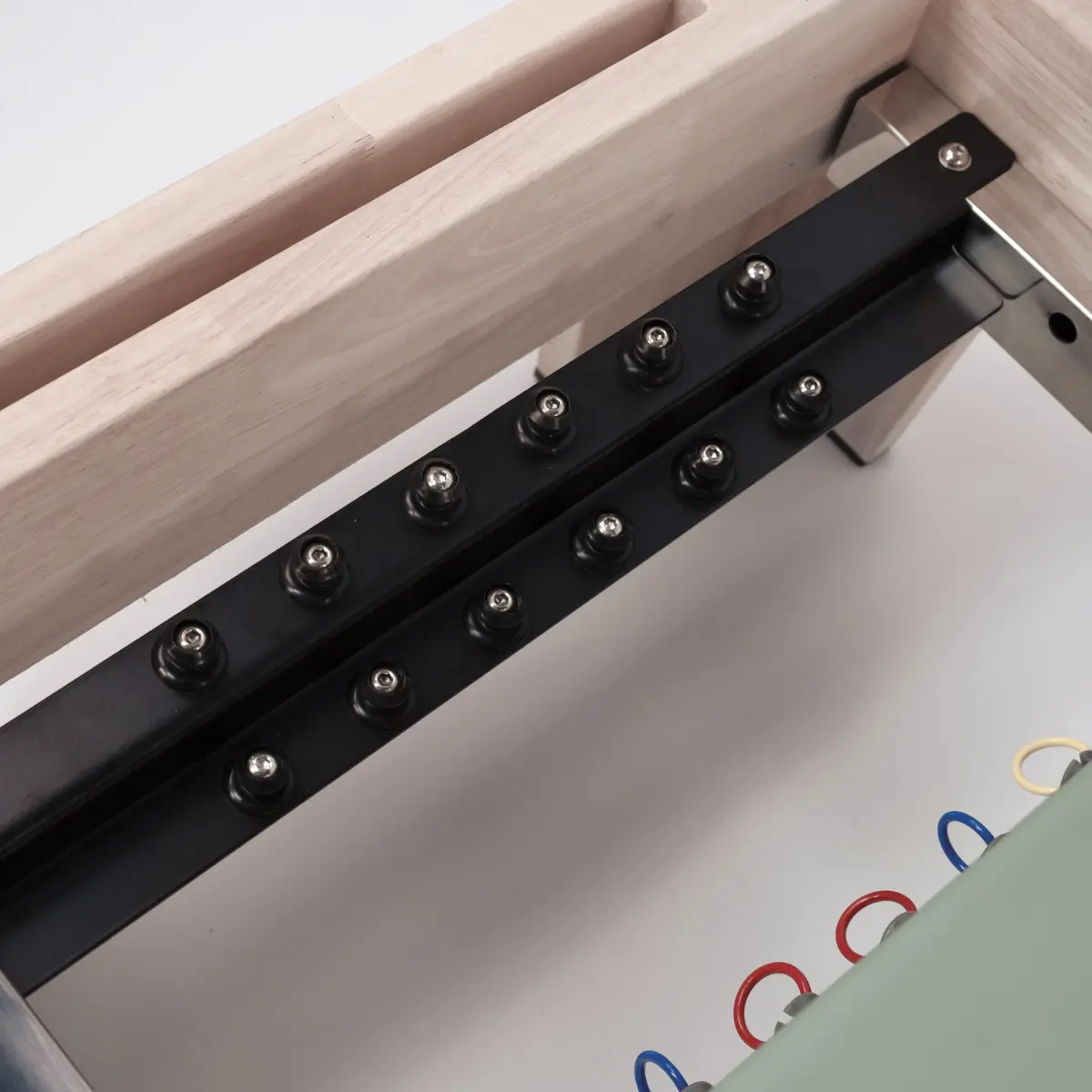 Close-up van een bedframe-mechanisme, zwarte metalen staven met klinknagels, verbonden met een houten frame en een lichtgroene basis.