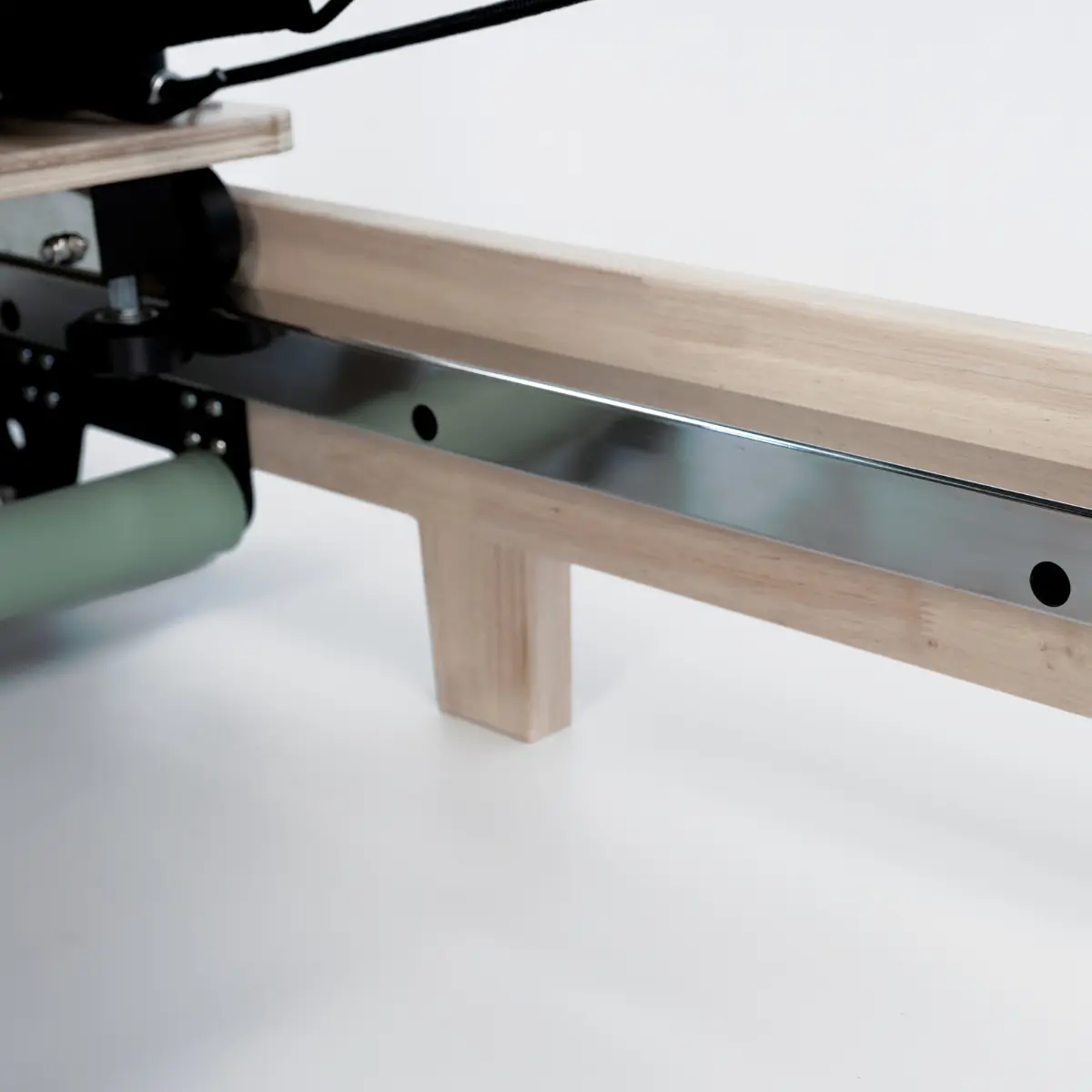 Detail van een houten roeimachine. Lichtbruin hout, een zilveren rail en een groene rol zijn zichtbaar tegen een witte achtergrond.