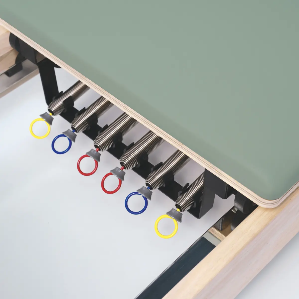 Een Pilates reformer machine met veren en gekleurde lussen. Groen platform, houten frame en metalen veren zijn zichtbaar.