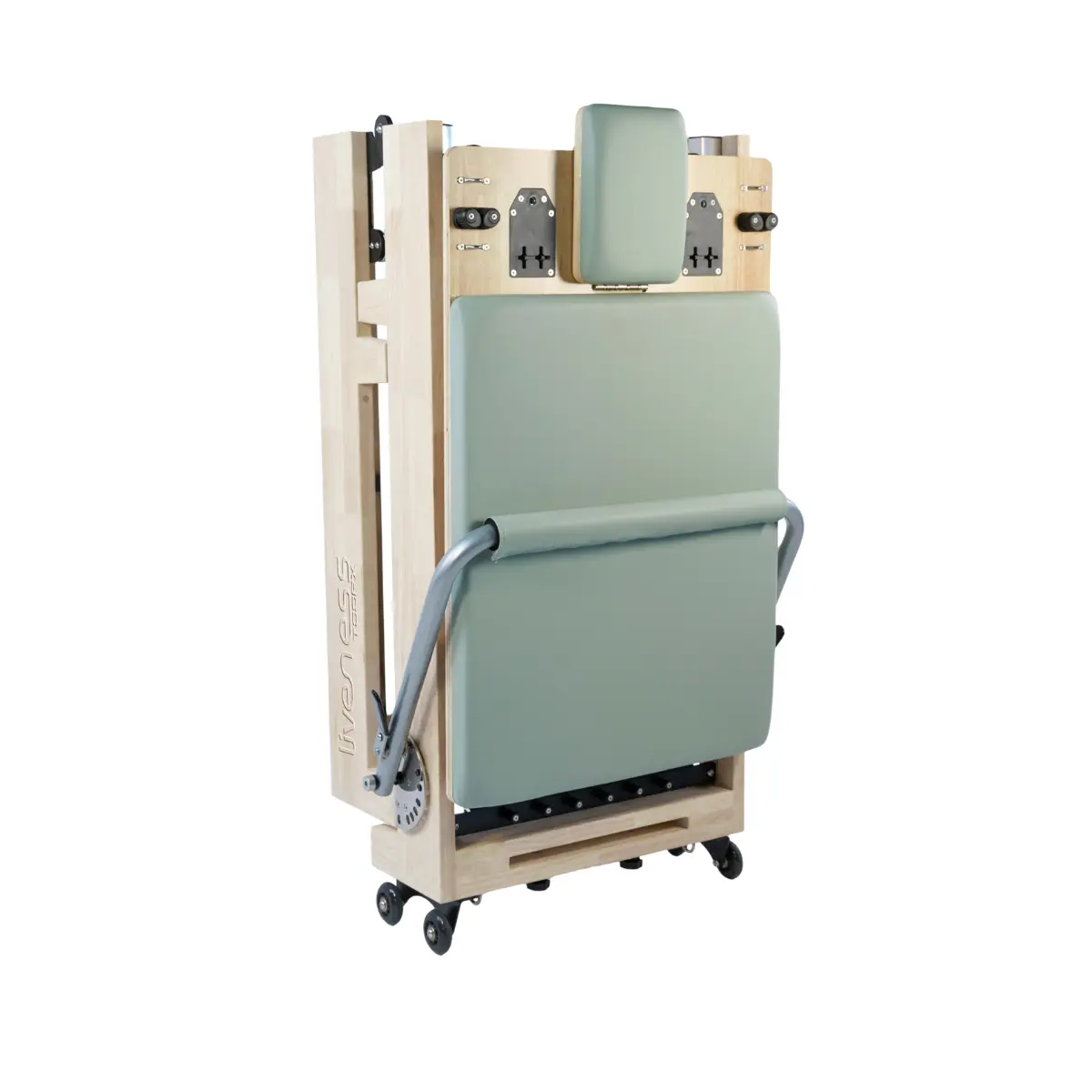 Een houten Pilates reformer met een groene gewatteerde zitting, hoofdsteun en metalen stang. Het heeft wielen en staat op een witte achtergrond.
