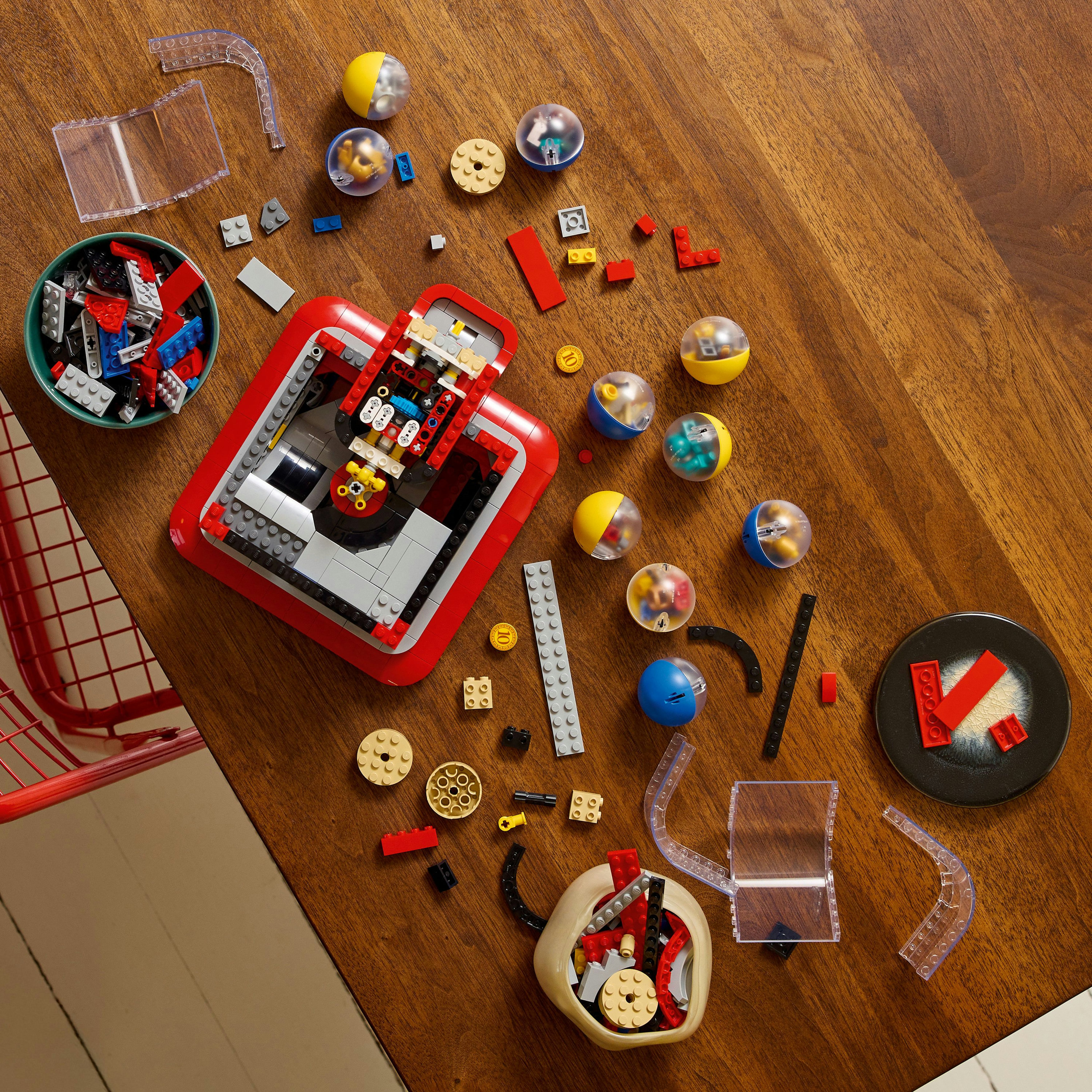 Drewniany stół z klockami Lego, miskami z klockami i przezroczystymi elementami z tworzywa sztucznego. Obecnych jest również kilka kul Lego.