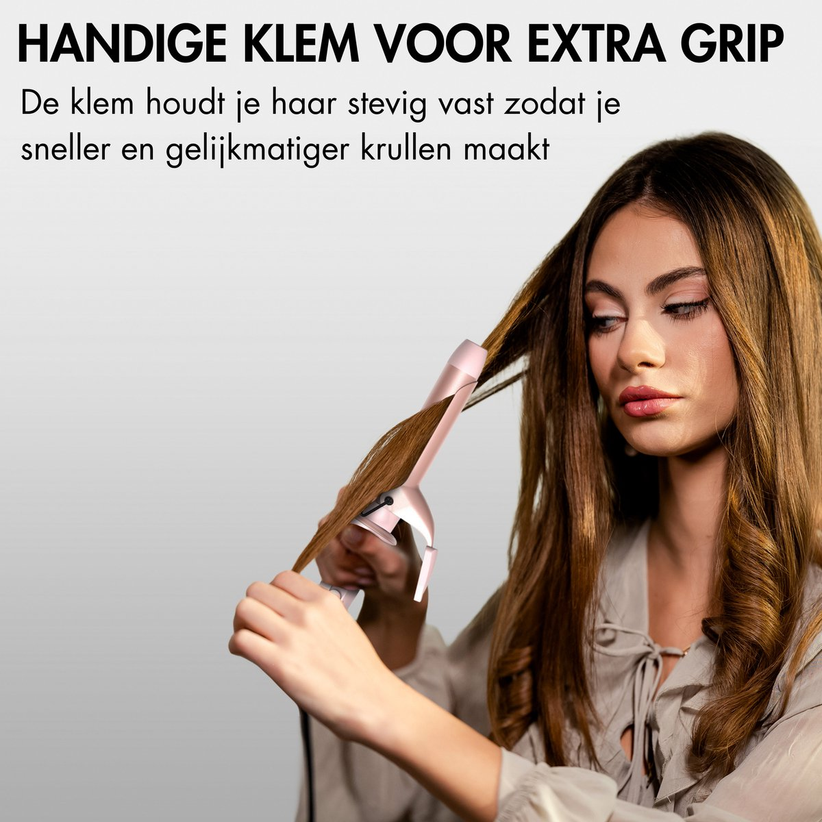 Een vrouw krult haar haar met een roze krultang. Haar haar is bruin en ze draagt een lichtgekleurde blouse.