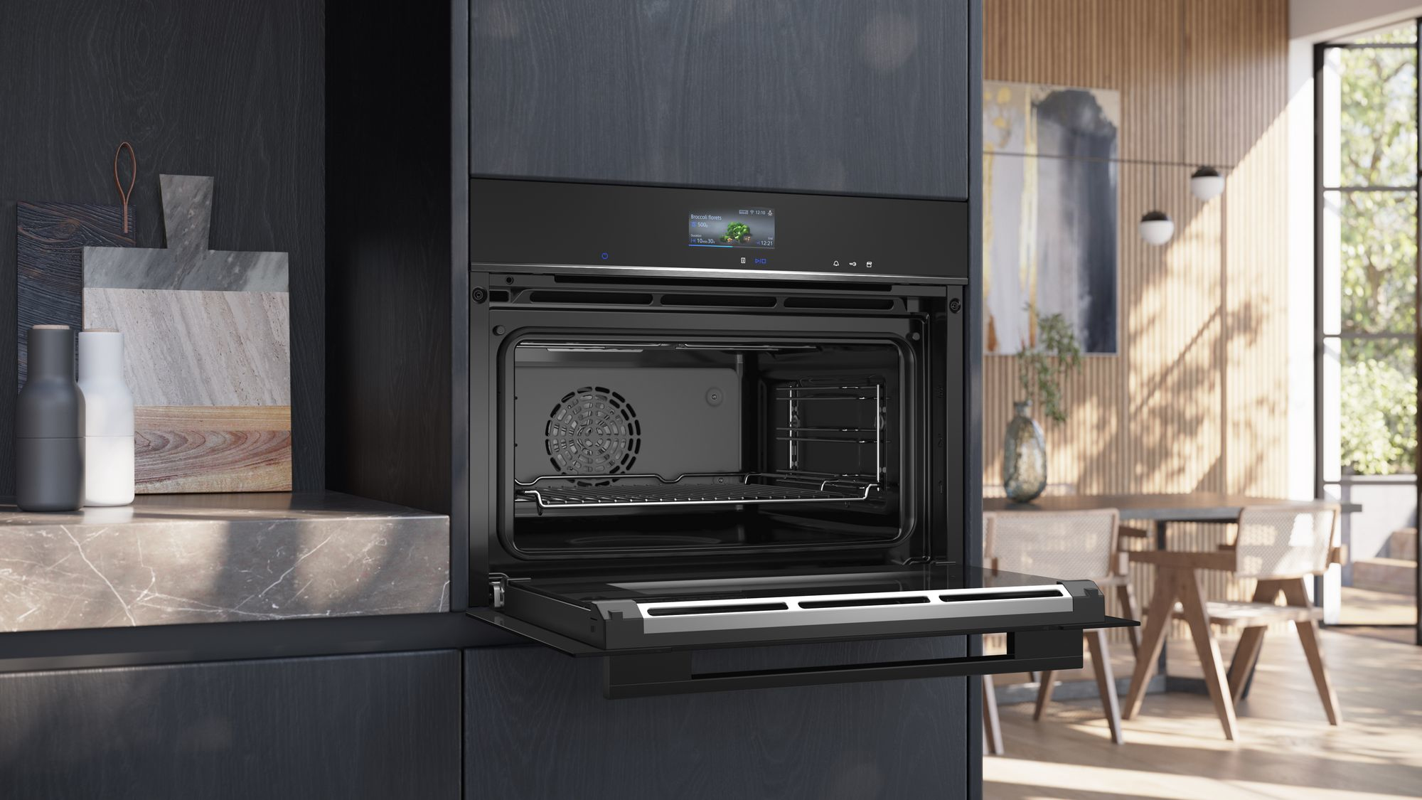 Een open zwarte oven in een moderne keuken. Binnenin zijn een rek en een ventilator zichtbaar. De achtergrond toont een eetgedeelte.