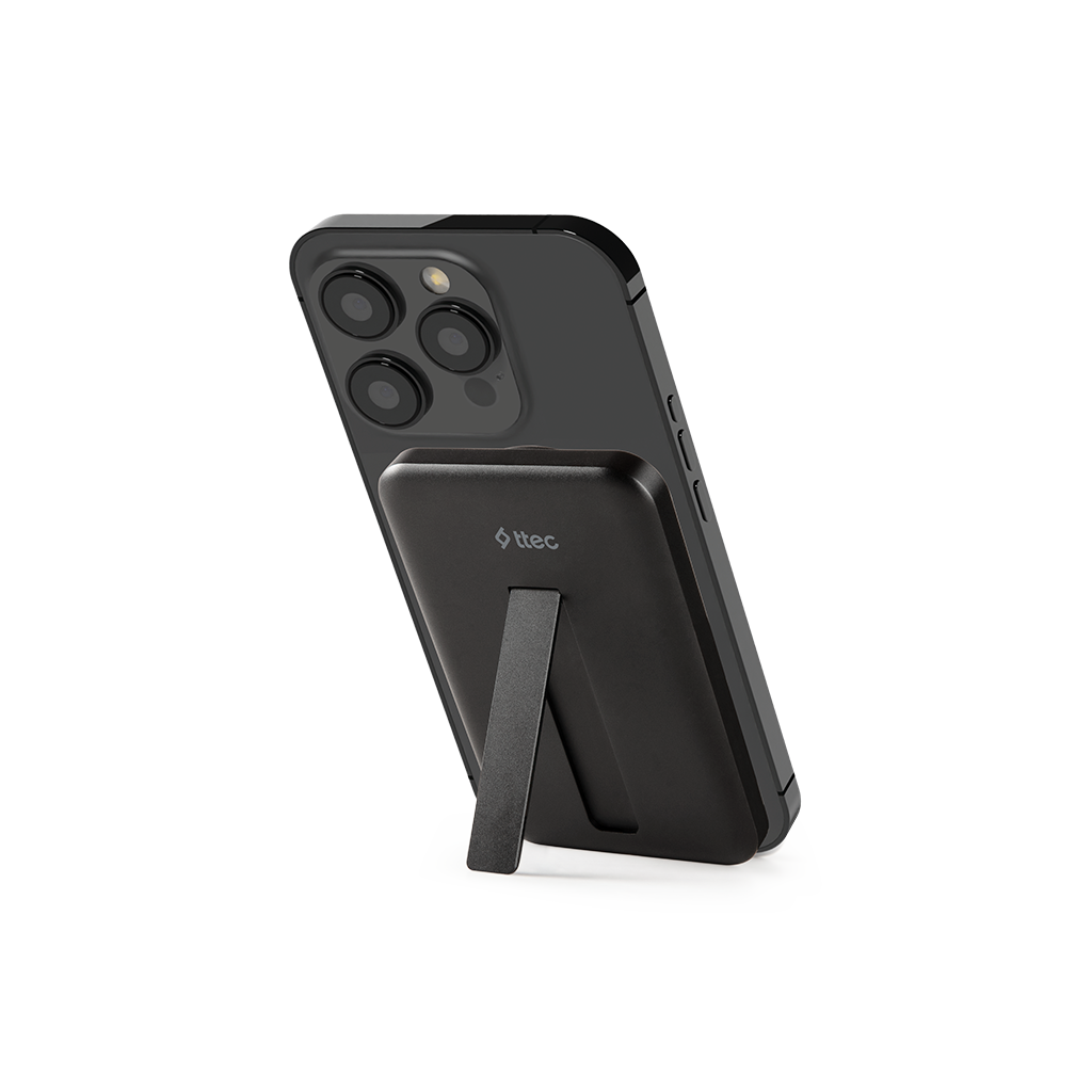 Siyah bir iPhone, siyah manyetik bir şarj cihazı takılı ve bir stand ile destekleniyor. Telefonda üç arka kamera var.