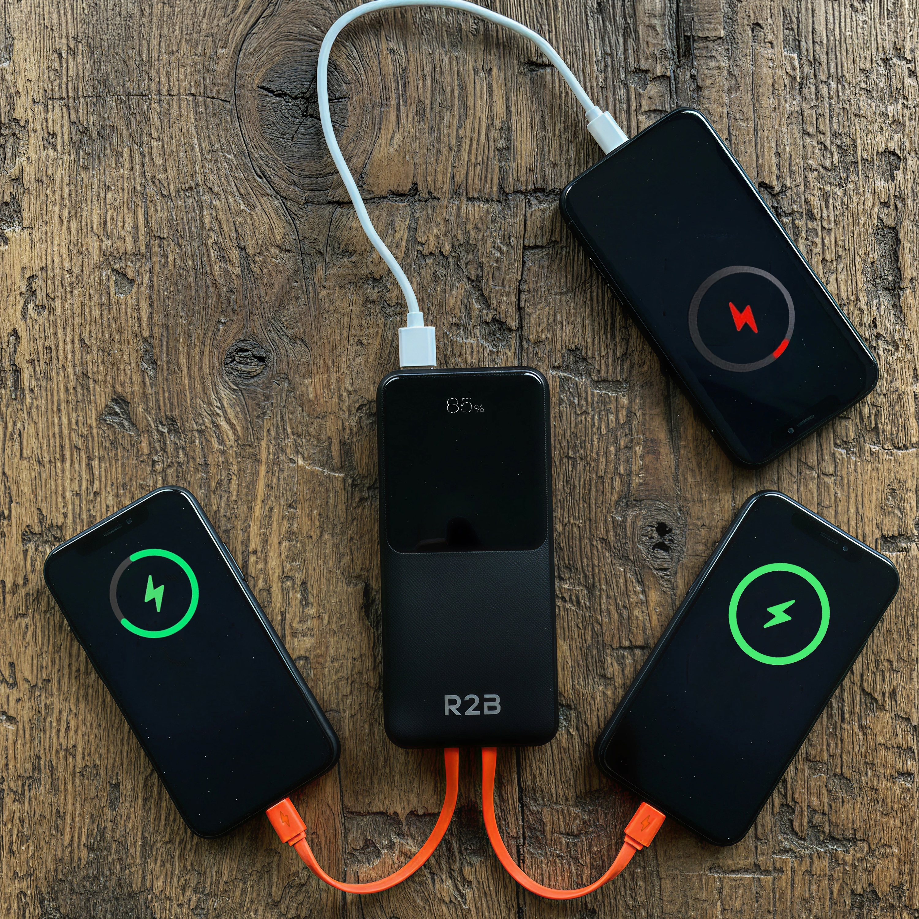 Trois téléphones se chargent à partir d'une banque d'alimentation noire sur une surface en bois. Deux ont des icônes de chargement vertes, une rouge.