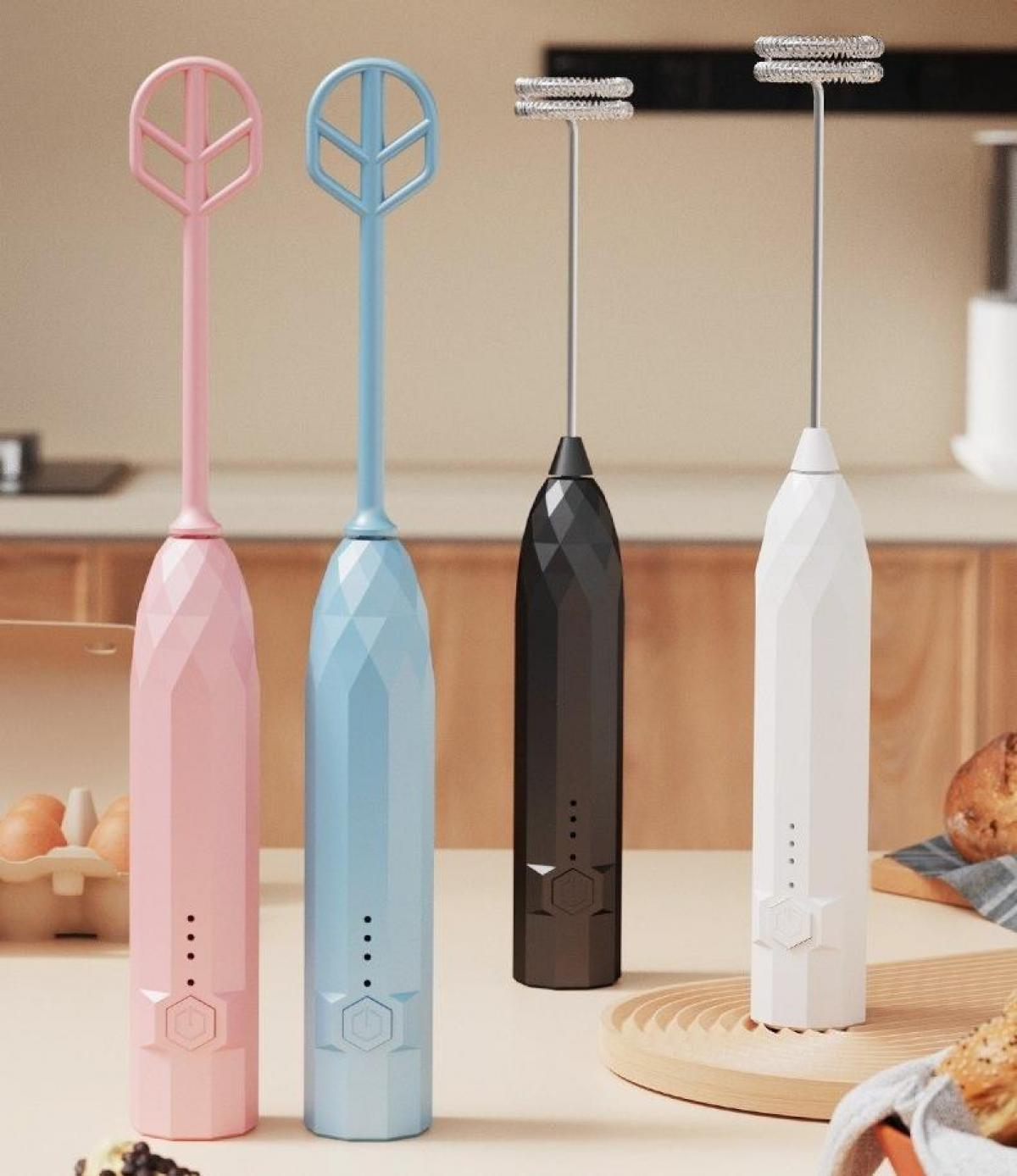 Vier bunte Milchaufschäumer. Rosa und blau haben dekorative Aufsätze, schwarz und weiß haben Aufschäumerköpfe. Küchenhintergrund.