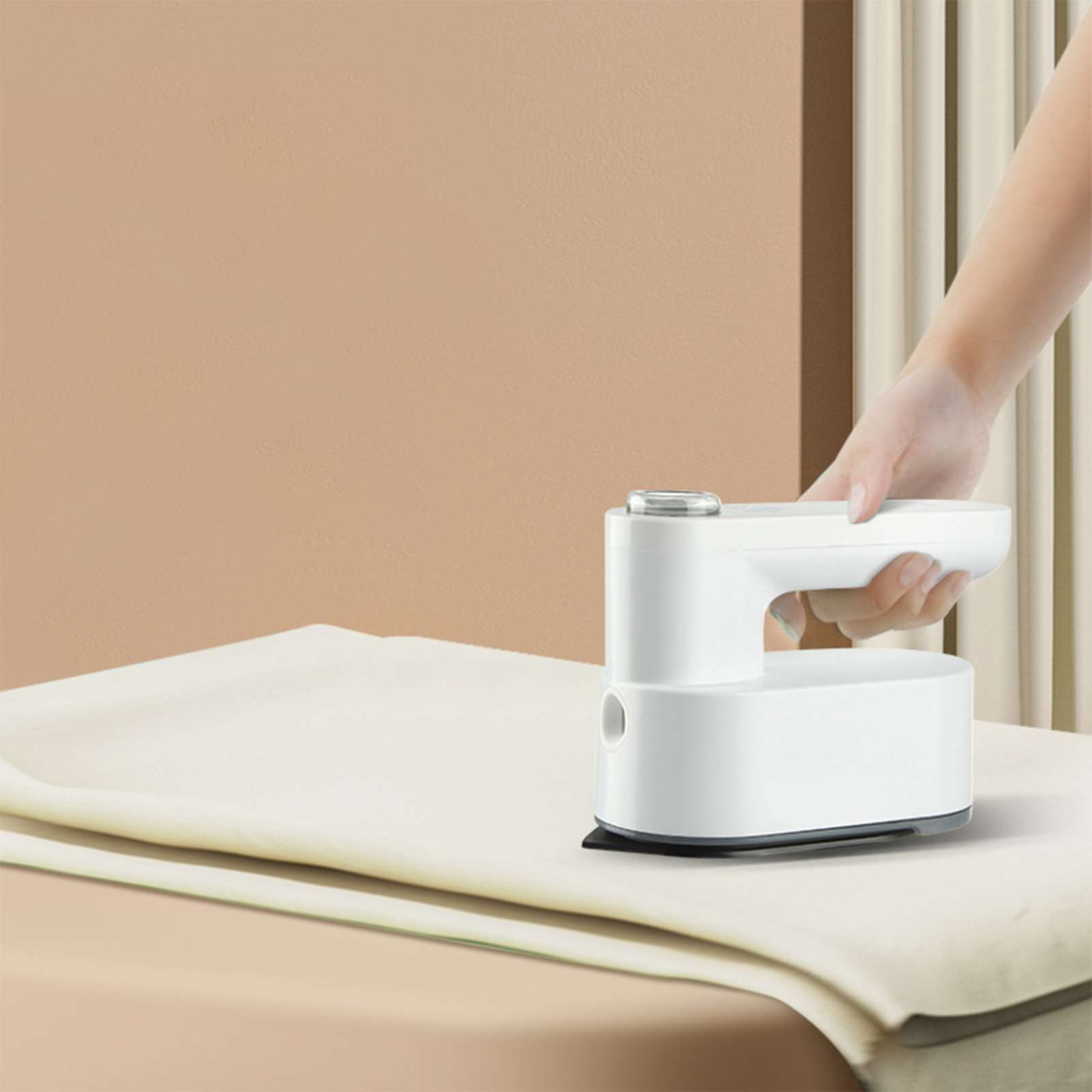 Eine Hand hält ein weißes Bügeleisen über einer beigen Oberfläche. Hintergrund: beige Wand und weiße Jalousien.