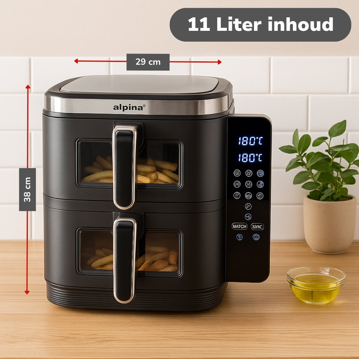 Een zwarte Alpina airfryer met friet in de manden. Hij is 29 cm breed en 38 cm hoog. Daarnaast een plant en een bakje olie.