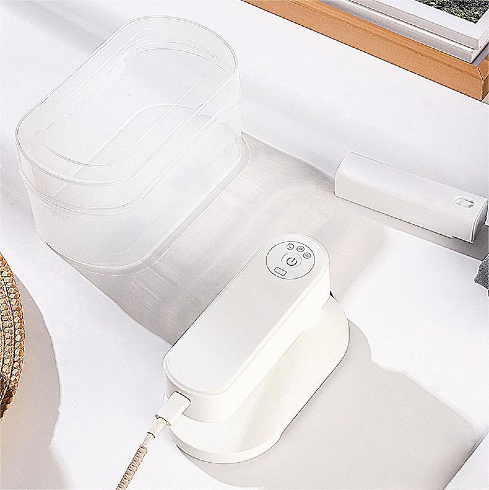 Weißes Mini-Bügeleisen mit Hülle und weißem zylindrischem Zubehör auf weißer Oberfläche. USB-Kabel ist angeschlossen.