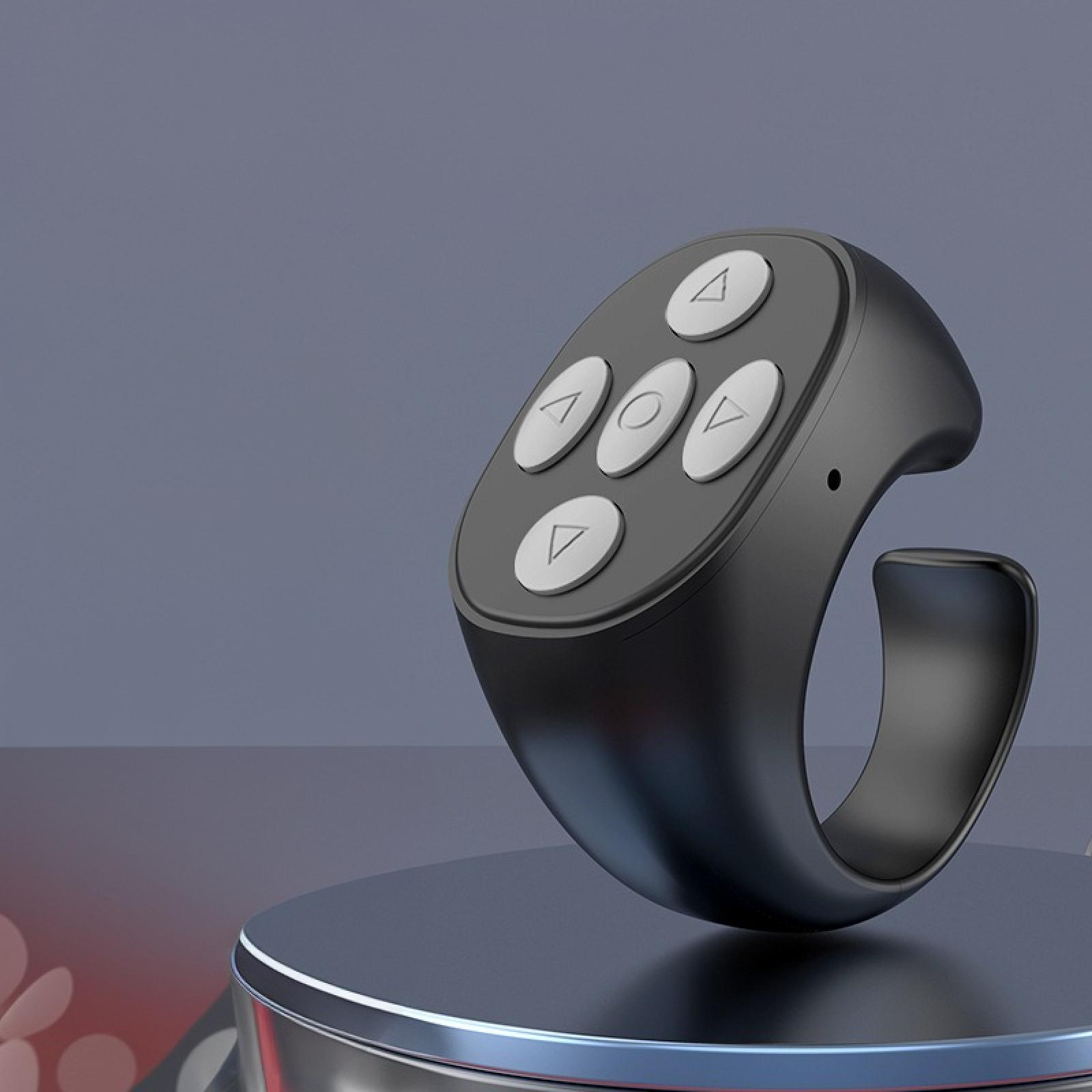 Eine schwarze ringförmige Fernbedienung mit fünf weißen Knöpfen auf einer grauen Plattform mit blauem Hintergrund.