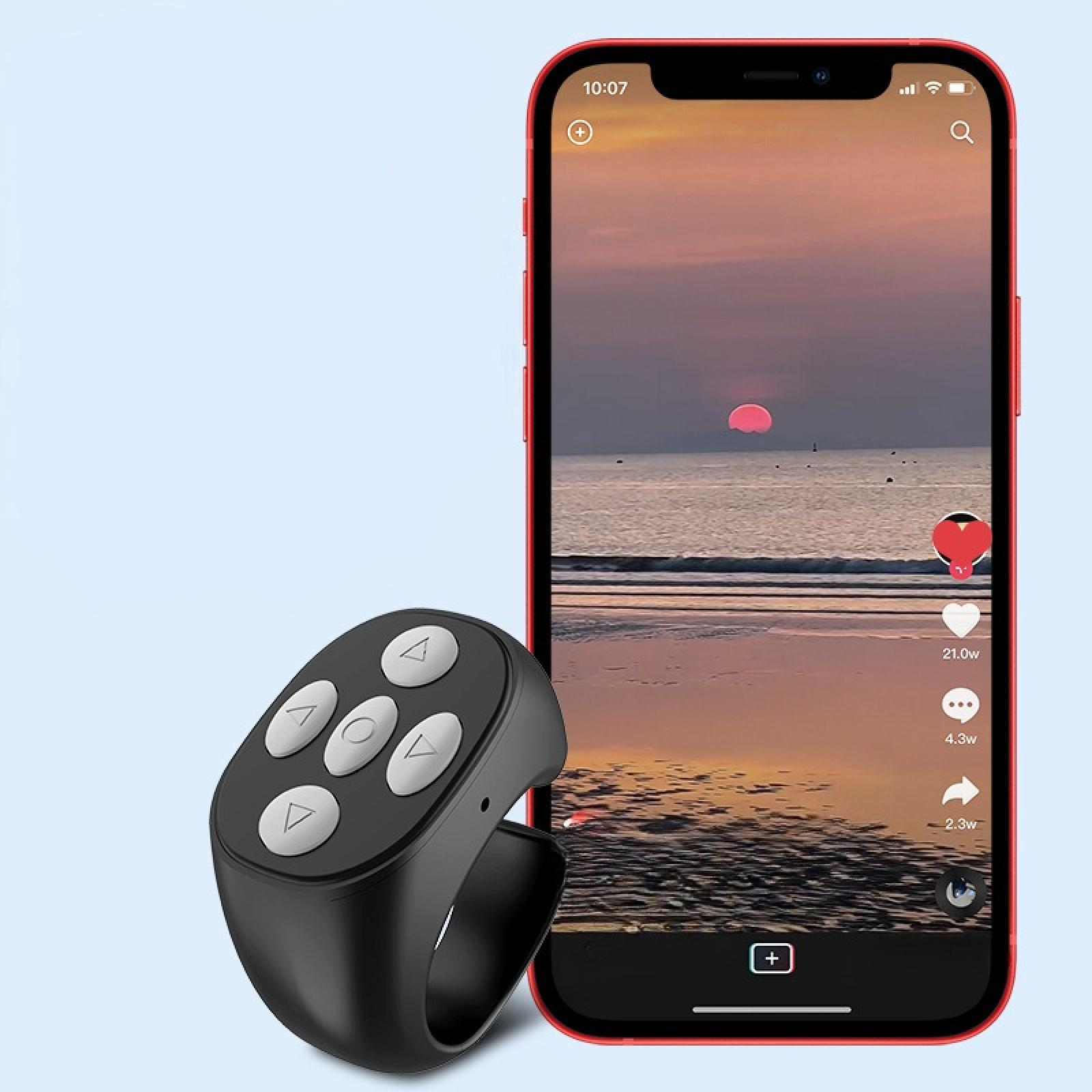 Ein schwarzer Fernbedienungsring mit weißen Knöpfen neben einem Telefon, das einen Sonnenuntergang über dem Meer zeigt.