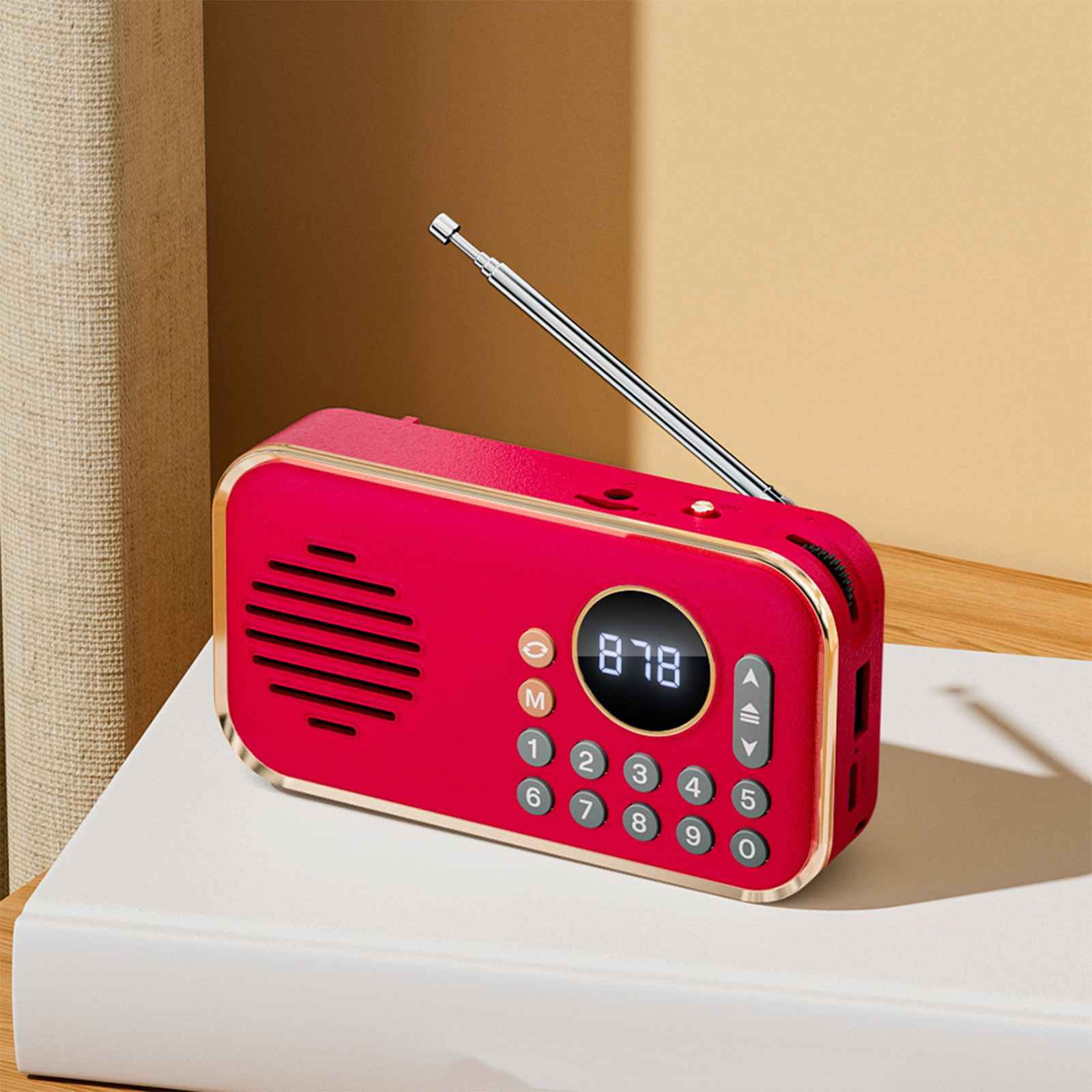 Ein rotes Radio mit silberner Antenne steht auf einer weißen Oberfläche. Es hat eine Digitalanzeige und nummerierte Tasten. Der Hintergrund ist warm.