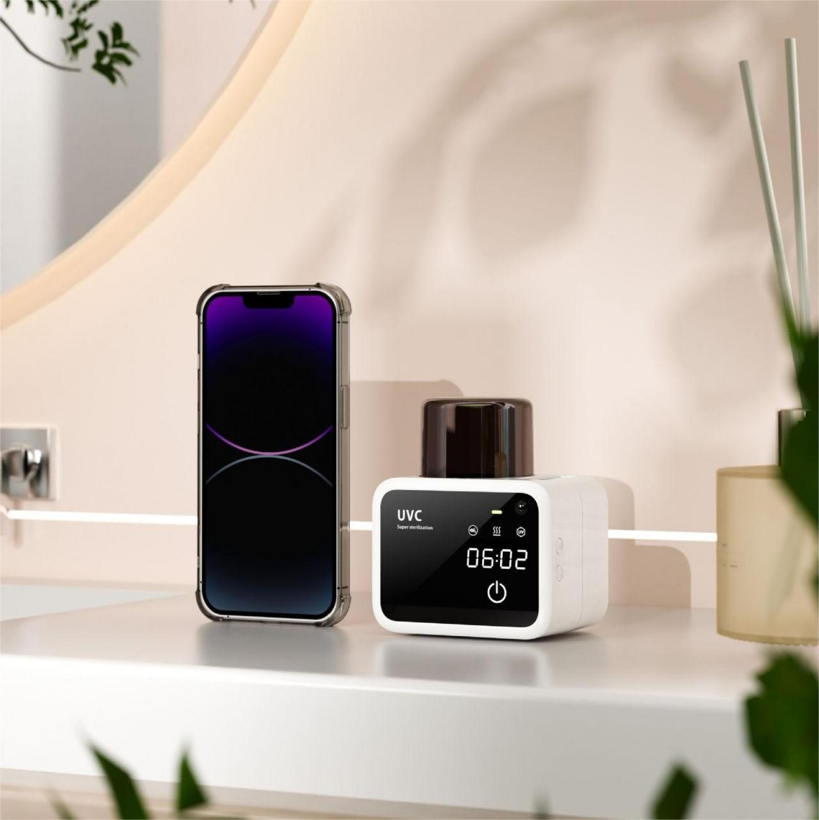 Ein Telefon und ein weißer UVC-Sterilisator stehen auf einer weißen Oberfläche. Das Telefon hat einen schwarzen Bildschirm, der Sterilisator ein Display.