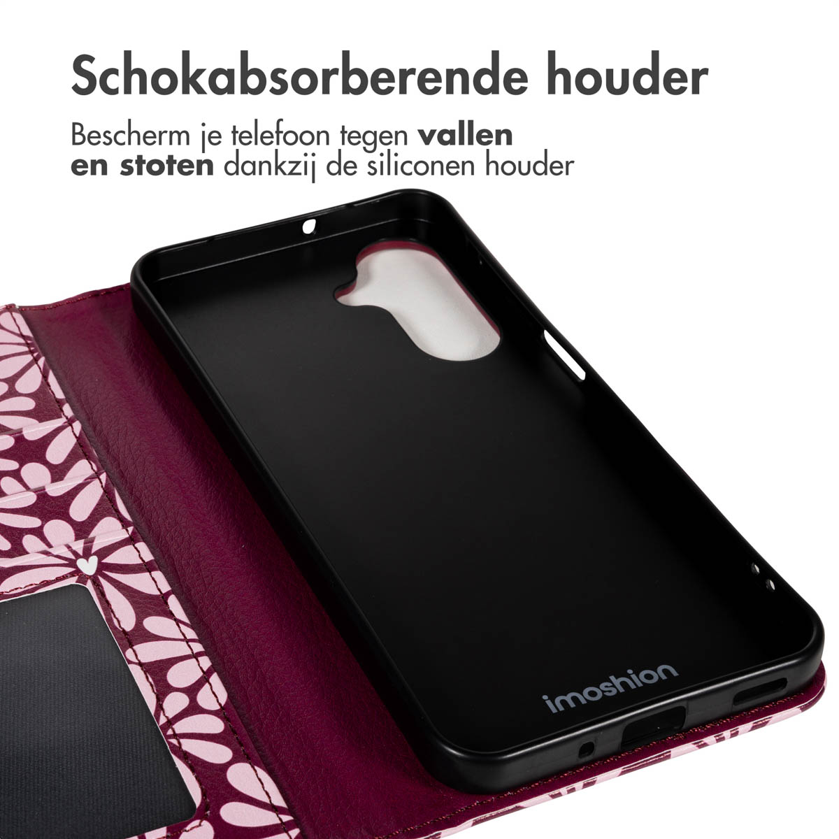 Un étui de téléphone noir est ouvert, révélant son intérieur. L'étui est sur une couverture à motifs floraux. Le texte en haut dit 'Schokabsorberende houder'.