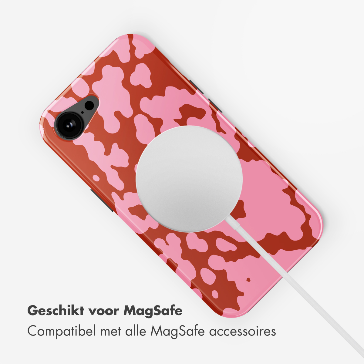 Een telefoon met een roze en bruine koeienprint hoes is verbonden met een witte MagSafe-oplader, op een wit oppervlak.