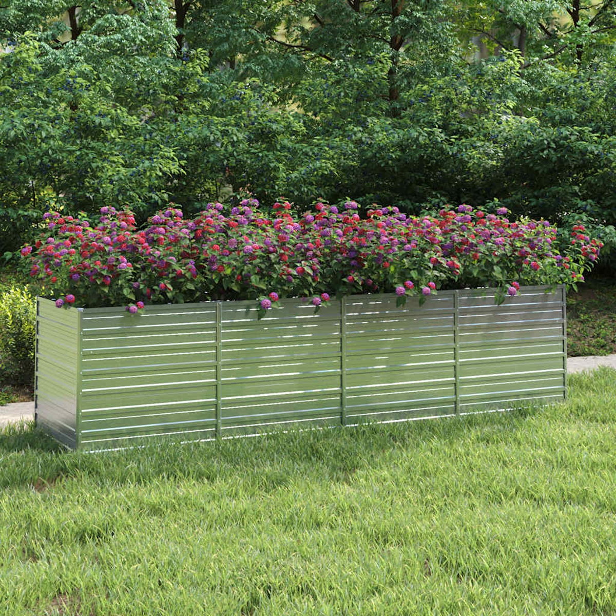 Ein metallischer Pflanzkasten enthält leuchtend rosa und lila Blumen. Er steht auf Gras, mit Bäumen im Hintergrund.