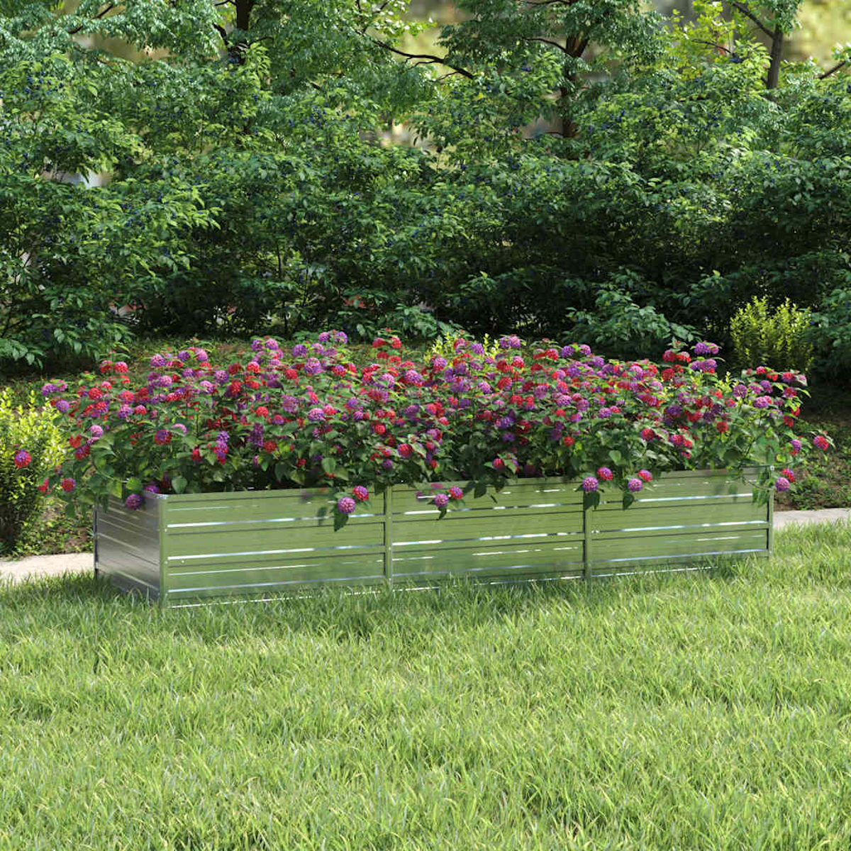 Eine Metallpflanzkasten mit leuchtend roten und lila Blumen steht auf grünem Gras, mit üppigen grünen Büschen im Hintergrund.