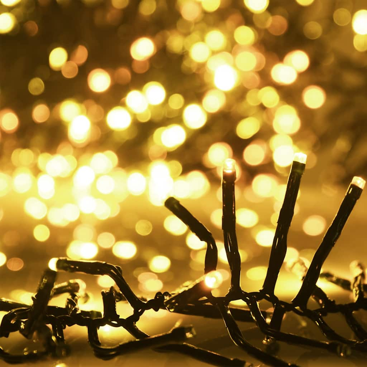 Nahaufnahme von Weihnachtslichtern. Fokus auf die schwarzen Drähte mit kleinen, hellweißen Lichtern. Verschwommene goldene Bokeh-Lichter im Hintergrund.