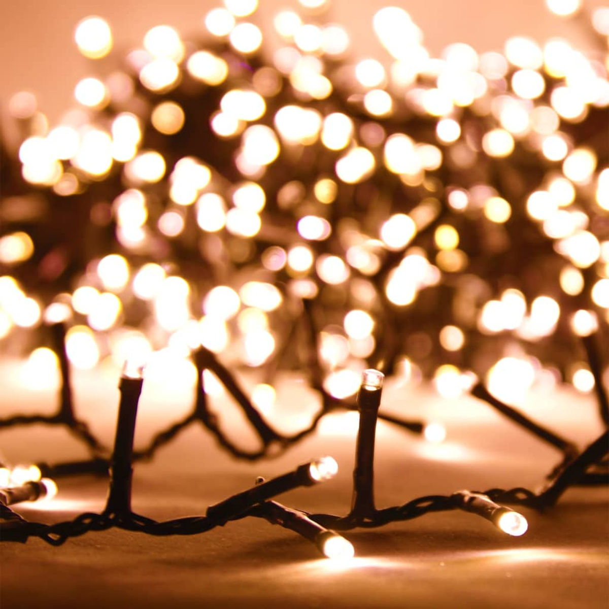 Nahaufnahme von warmweißen Weihnachtslichtern. Unscharfer Hintergrund mit ähnlichen Lichtern. Schwarze Drähte und kleine Glühbirnen sind scharf.