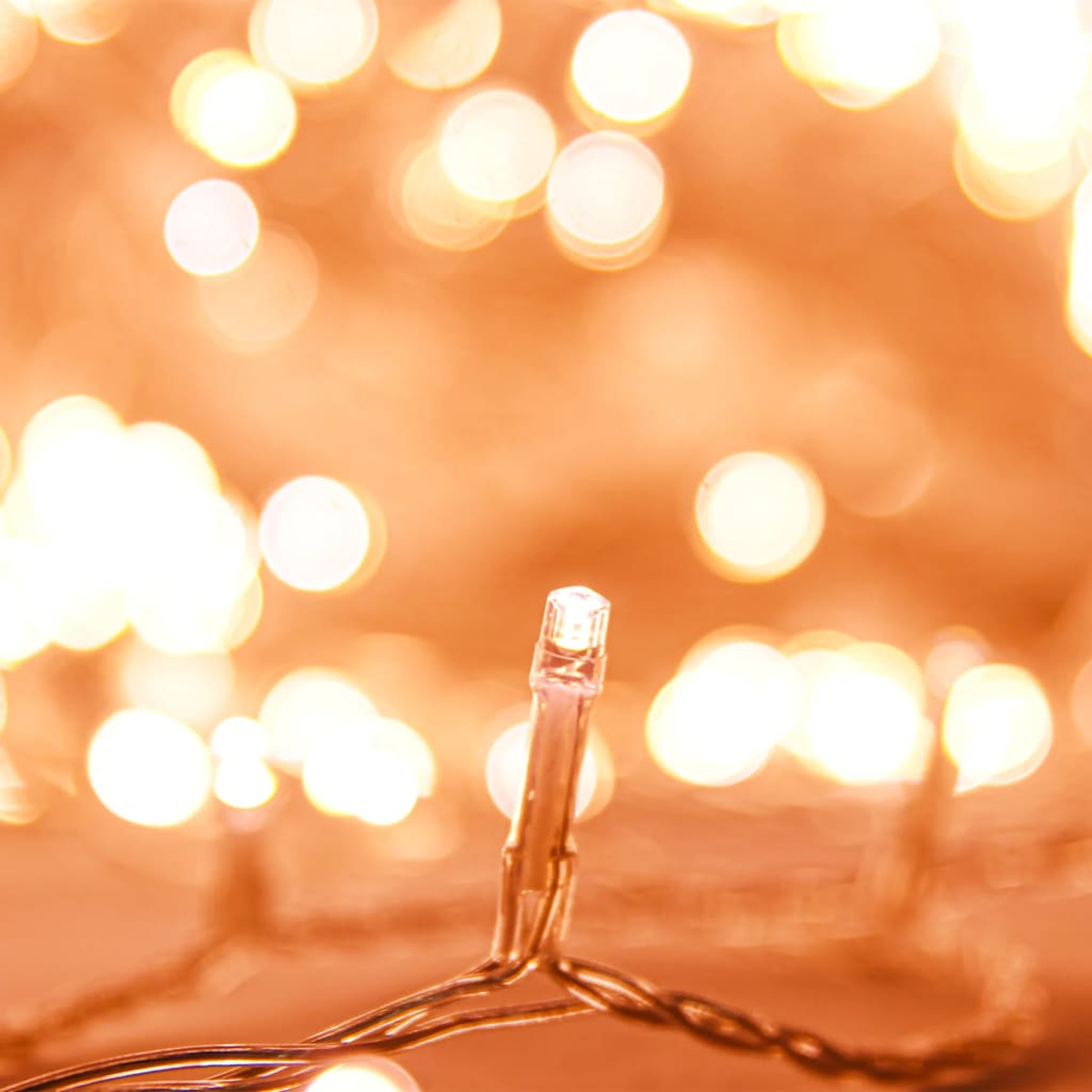 Nahaufnahme einer beleuchteten LED-Weihnachtsbeleuchtung mit unscharfem Hintergrund aus anderen Lichtern in warmen Tönen. Das Licht ist fokussiert.