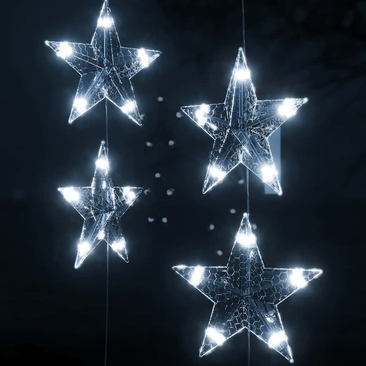 Vier beleuchtete sternförmige Dekorationen hängen vor einem dunklen Hintergrund. Jeder Stern hat helle weiße Lichter.