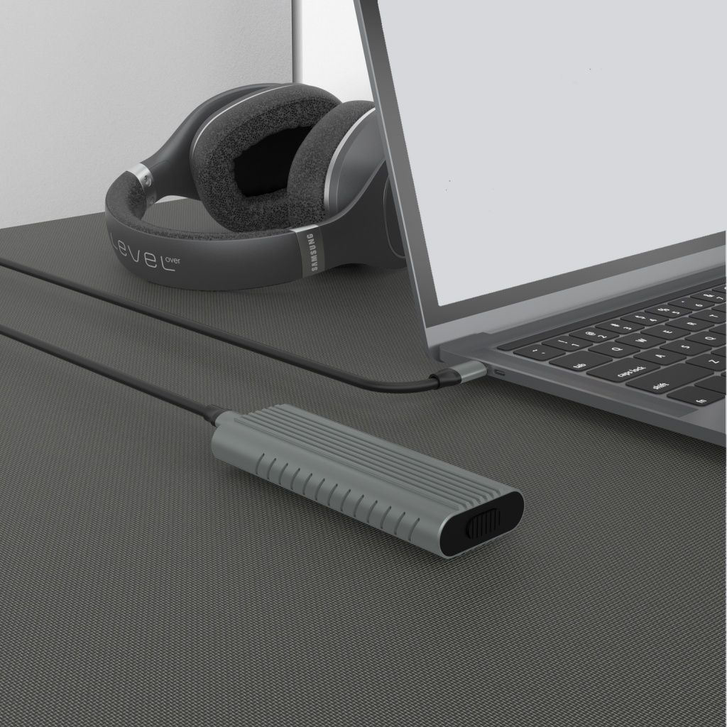 Un portátil, auriculares y un dispositivo gris sobre una superficie gris texturizada. Un cable conecta el dispositivo al portátil.