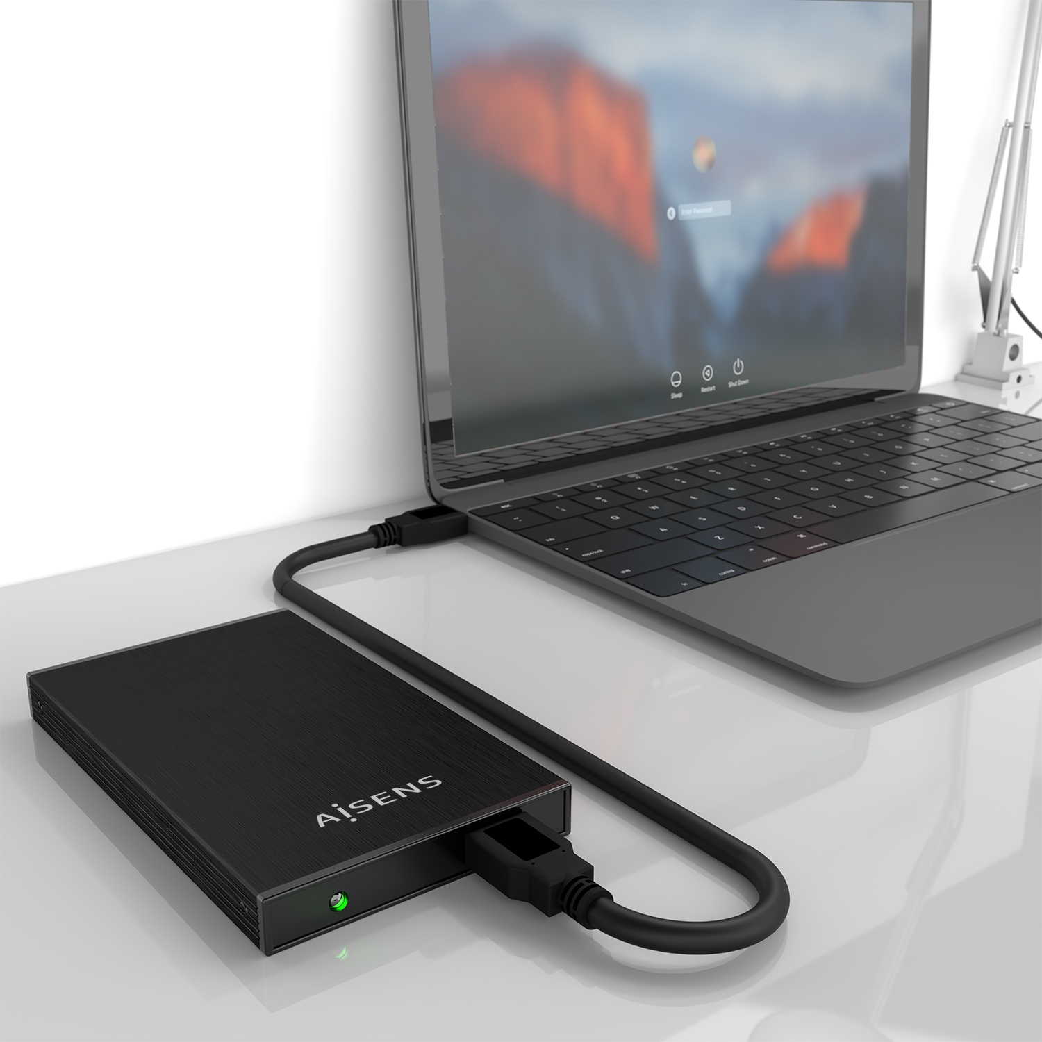 Un disco duro externo negro conectado a una computadora portátil. La pantalla de la computadora portátil muestra una pantalla de inicio de sesión. El escritorio es blanco.