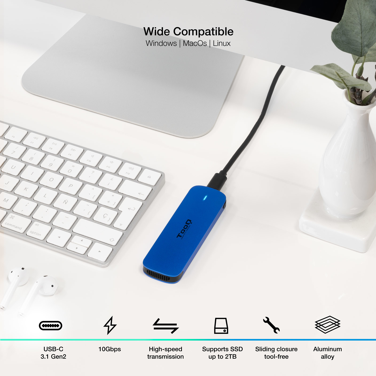 Un disco duro externo azul conectado a una computadora, con teclado y un jarrón blanco sobre un escritorio blanco.