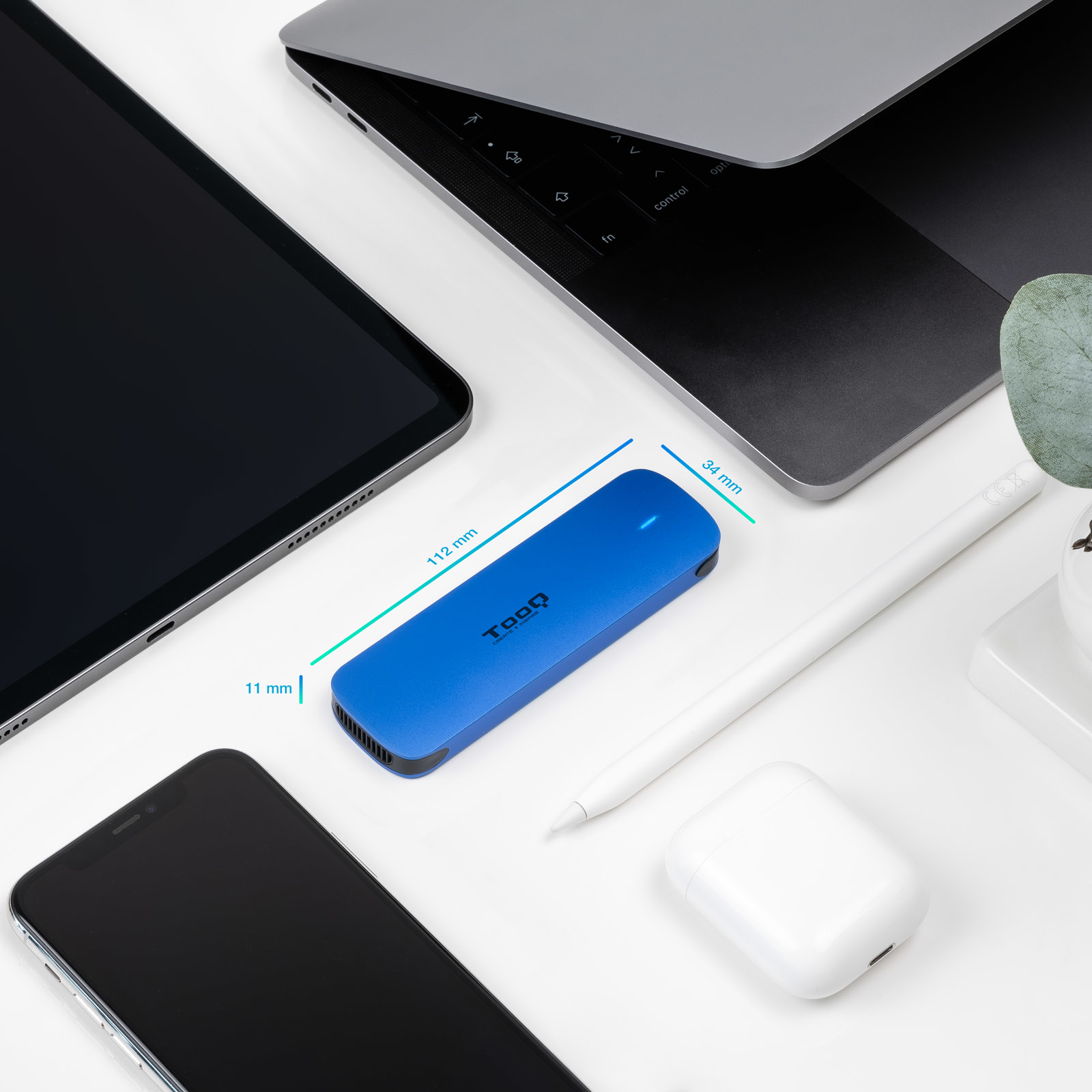 Un disco duro externo Toqq azul está rodeado por una computadora portátil, una tableta, un teléfono, AirPods y un lápiz óptico sobre una superficie blanca.
