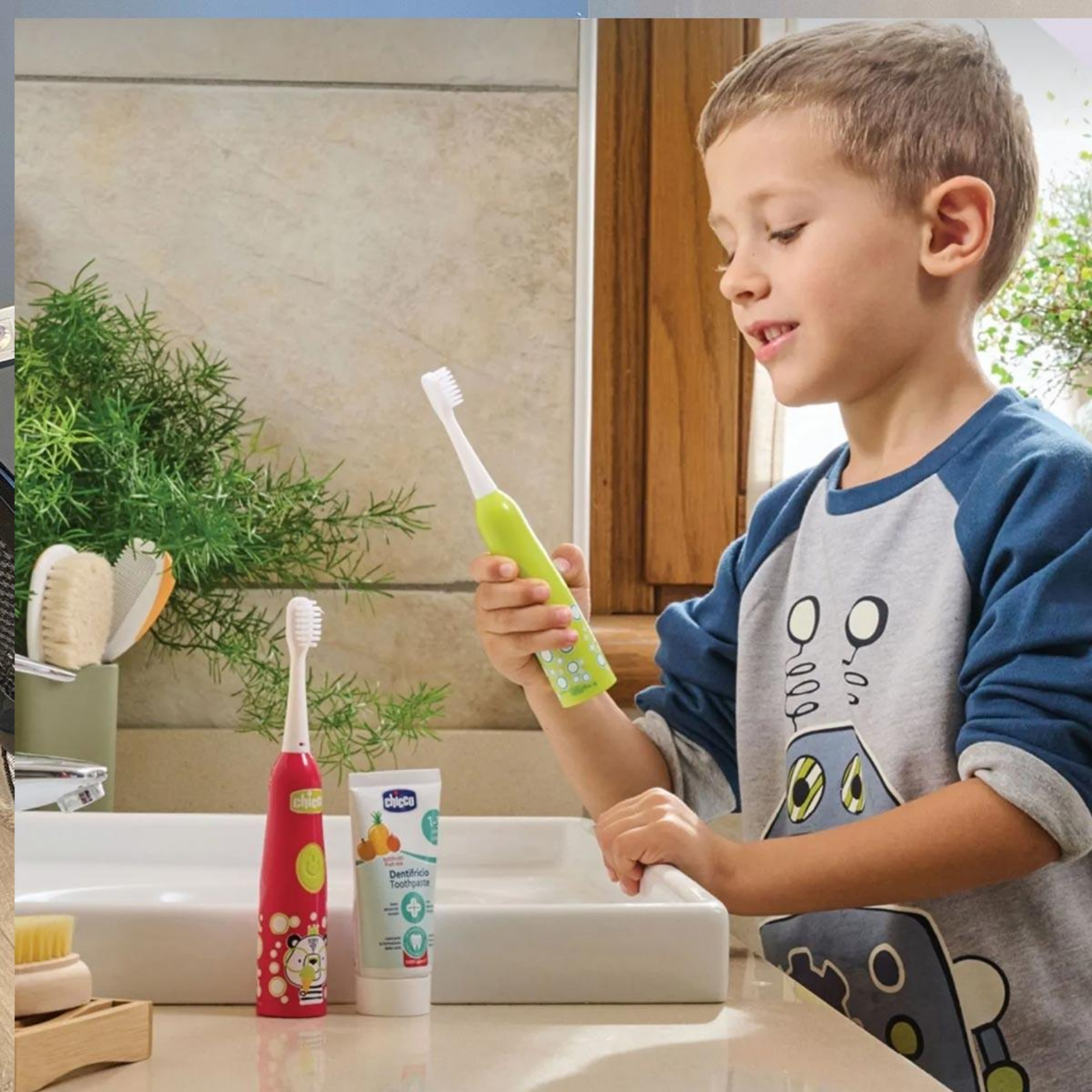 Un bambino in bagno tiene in mano uno spazzolino verde. Uno spazzolino rosso e dentifricio sono sul lavandino. Una pianta sullo sfondo.